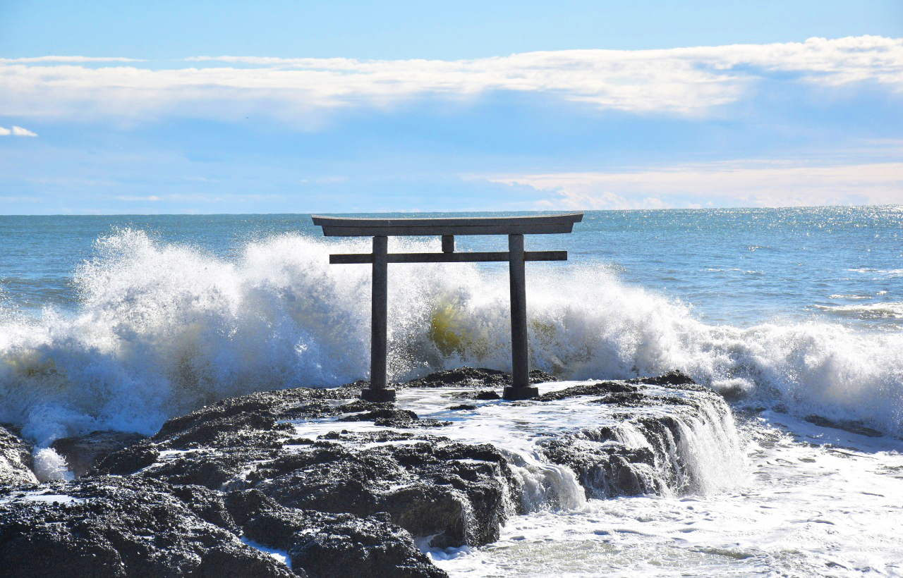 神磯鳥居矗立於礁岩之上,海浪拍岸飛濺水花,朱黑鳥居與遼闊海面相映,畫面莊嚴震撼,充滿神聖氣息。 神磯鳥居矗立於礁岩之上,海浪拍岸飛濺水花,朱黑鳥居與遼闊海面相映,畫面莊嚴震撼,充滿神聖氣息。