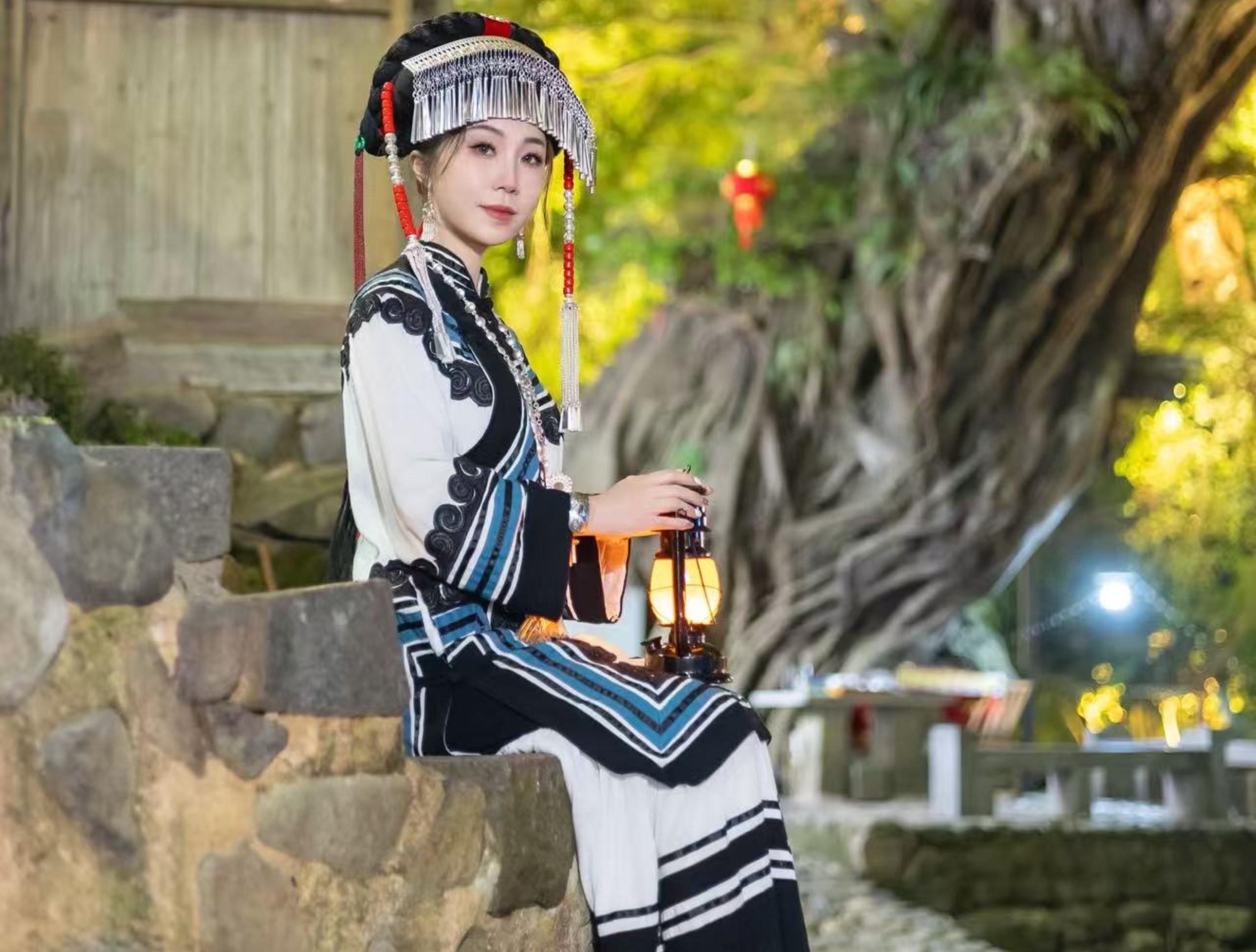 百年古榕的氣根垂在石階旁,身著黎風黑白紋樣服飾的姑娘靜坐著 百年古榕的氣根垂在石階旁,身著黎風黑白紋樣服飾的姑娘靜坐著