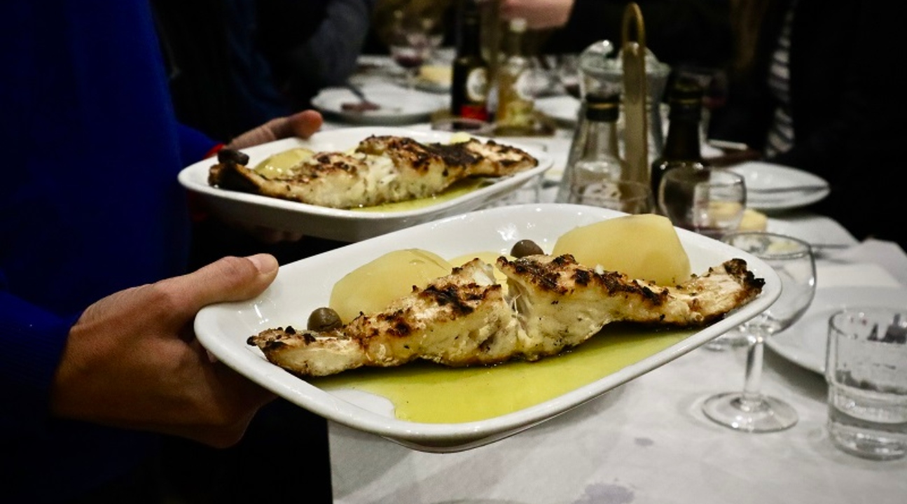 a Portuguese meal on a red bowl on top of a red plate; there's ham slices, greens, and potatoes on it