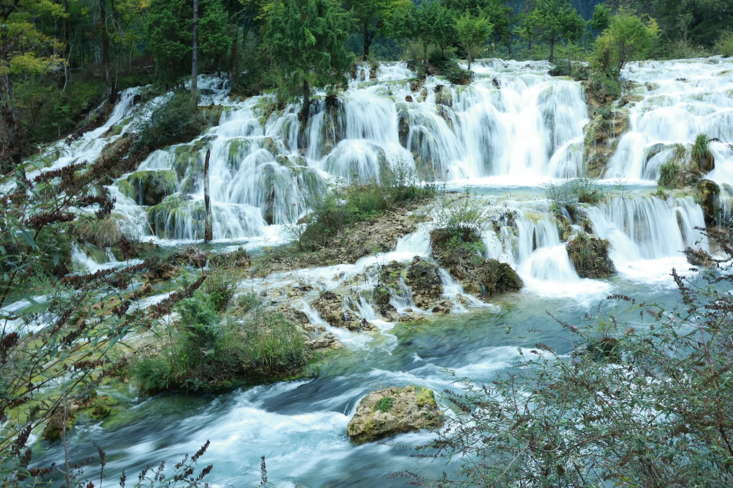 珍珠灘：日則溝大型鈣華灘，86 版《西遊記》經典取景地。平緩乳黃灘面，清流漫過坑窪濺起萬顆珍珠，陽光之下晶瑩閃爍。灘邊灌叢叢生，水聲潺潺，末端奔湧成新月形瀑布，水霧騰空，涼意沁心，是動態水景的絕佳觀賞點。