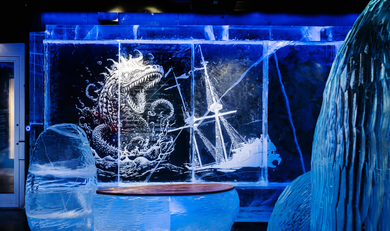 An intricately carved ice sculpture of an animal figure shines under colorful ambient lighting