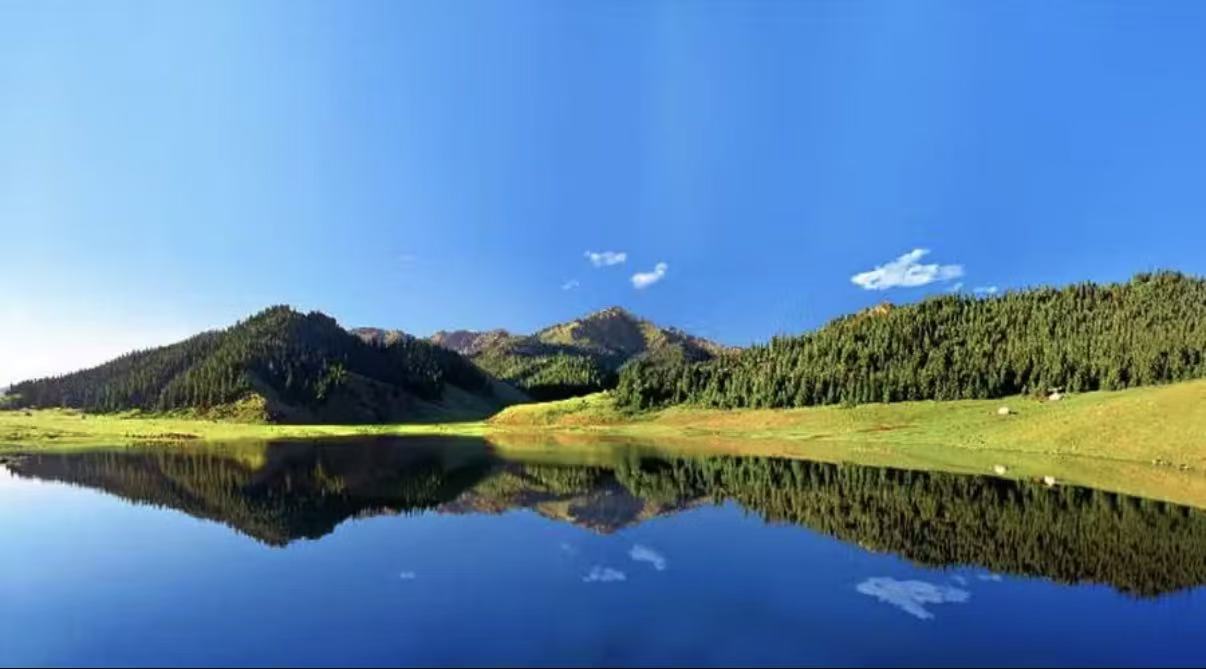 澄澈湖水如鏡面完整復刻山林與雲天，平緩草甸環繞湖畔，兩側山林層次分明。澄澈藍天浮著碎雲，遠山覆滿深綠林木，山水倒影渾然一體，靜謐遼闊，宛若不染塵囂的秘境