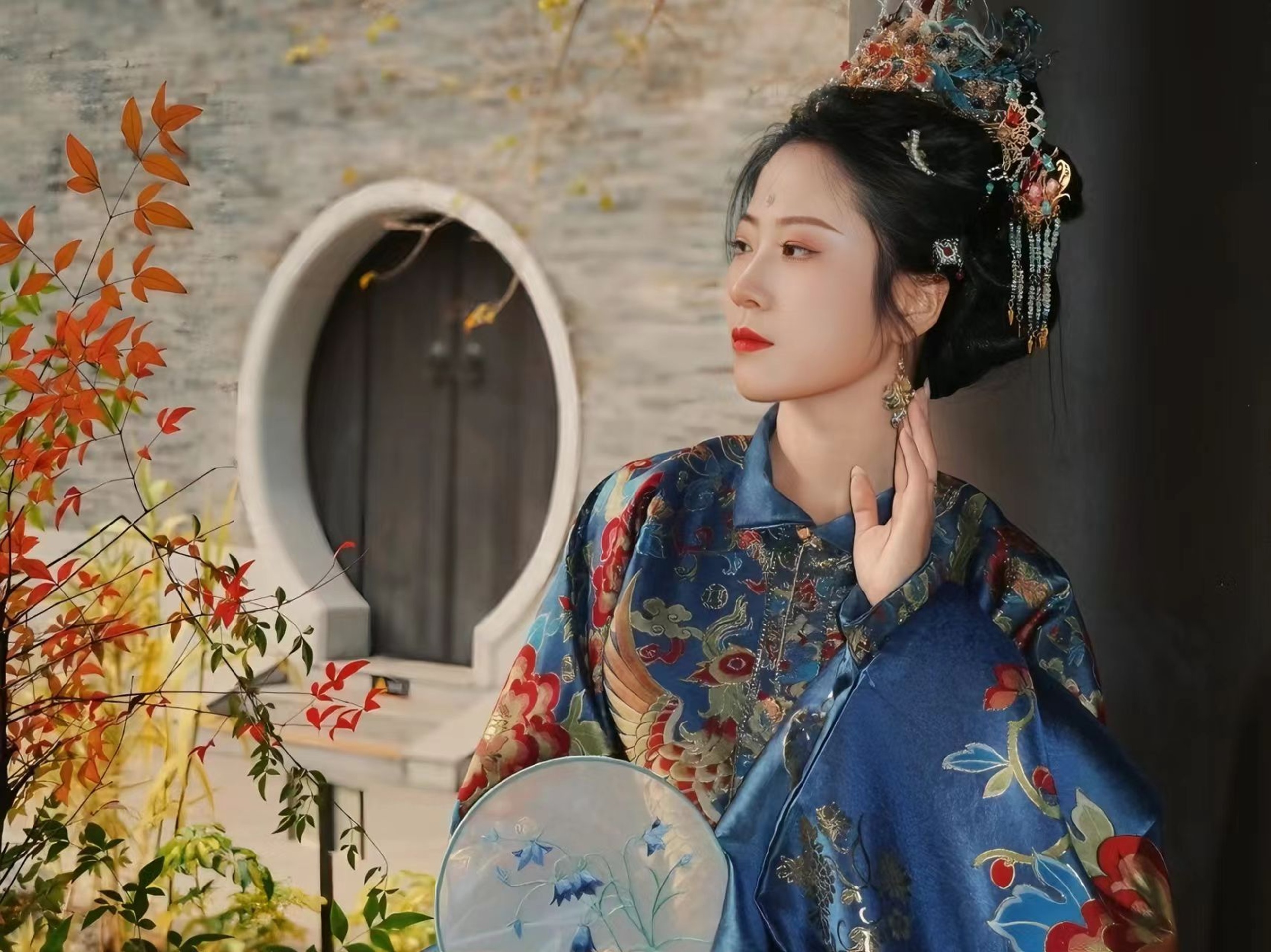 寶藍織金漢服配華麗鳳冠,少女持團扇立於圓門前,紅葉相映,盡顯明代貴婦的雍容與端莊 寶藍織金漢服配華麗鳳冠,少女持團扇立於圓門前,紅葉相映,盡顯明代貴婦的雍容與端莊