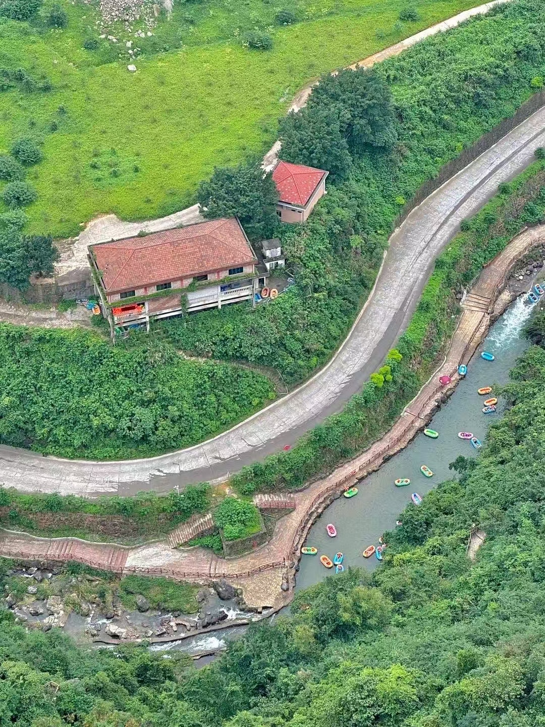 高空俯瞰黃騰峽漂流河道！蜿蜒峽谷間，彩色皮筏艇順流而下，兩岸青山疊翠、草木蔥蘢，蜿蜒公路與山間小屋相映，盡顯原生態峽谷漂流的壯闊與清涼