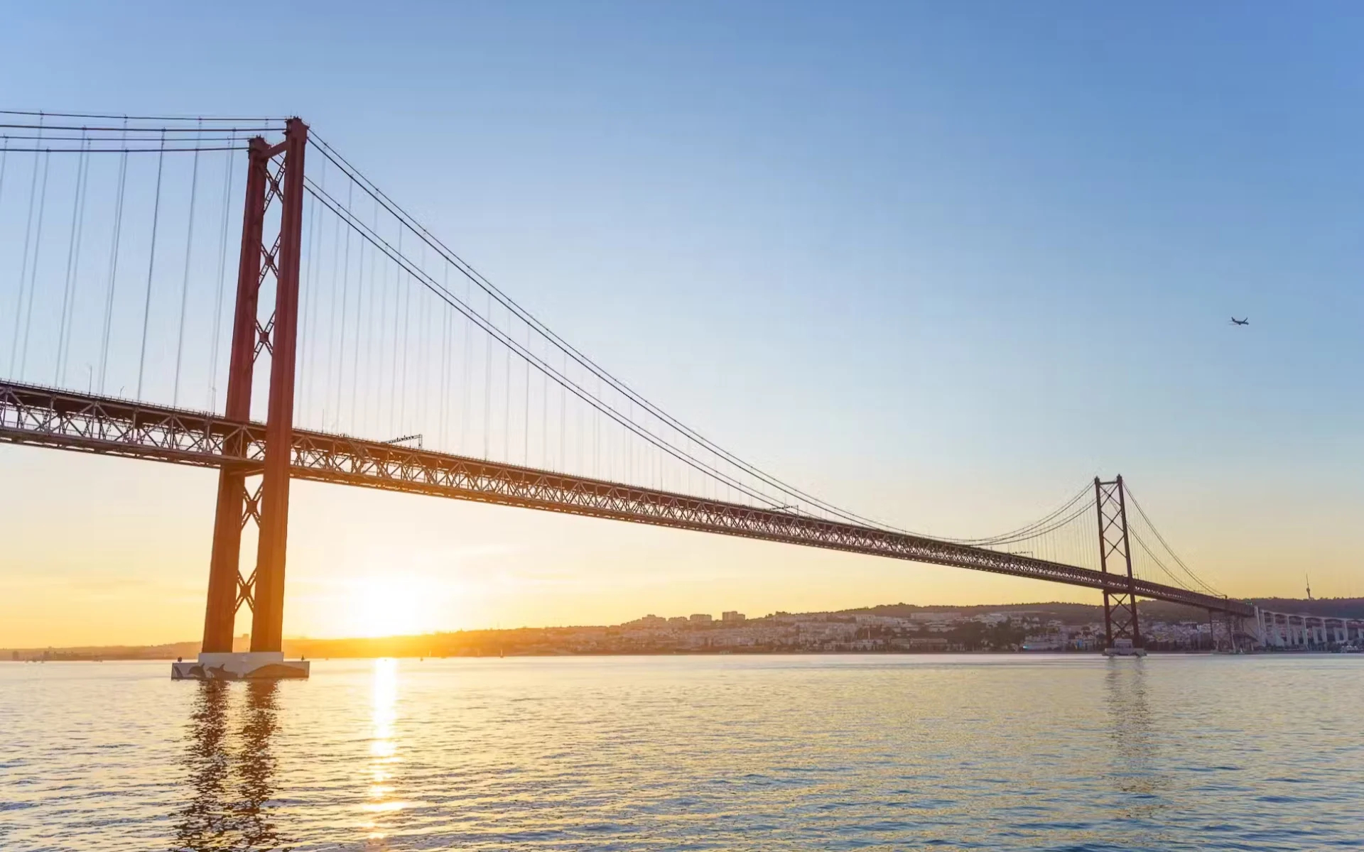 Admire Lisbon’s 25 de Abril Bridge glowing in the evening sunset