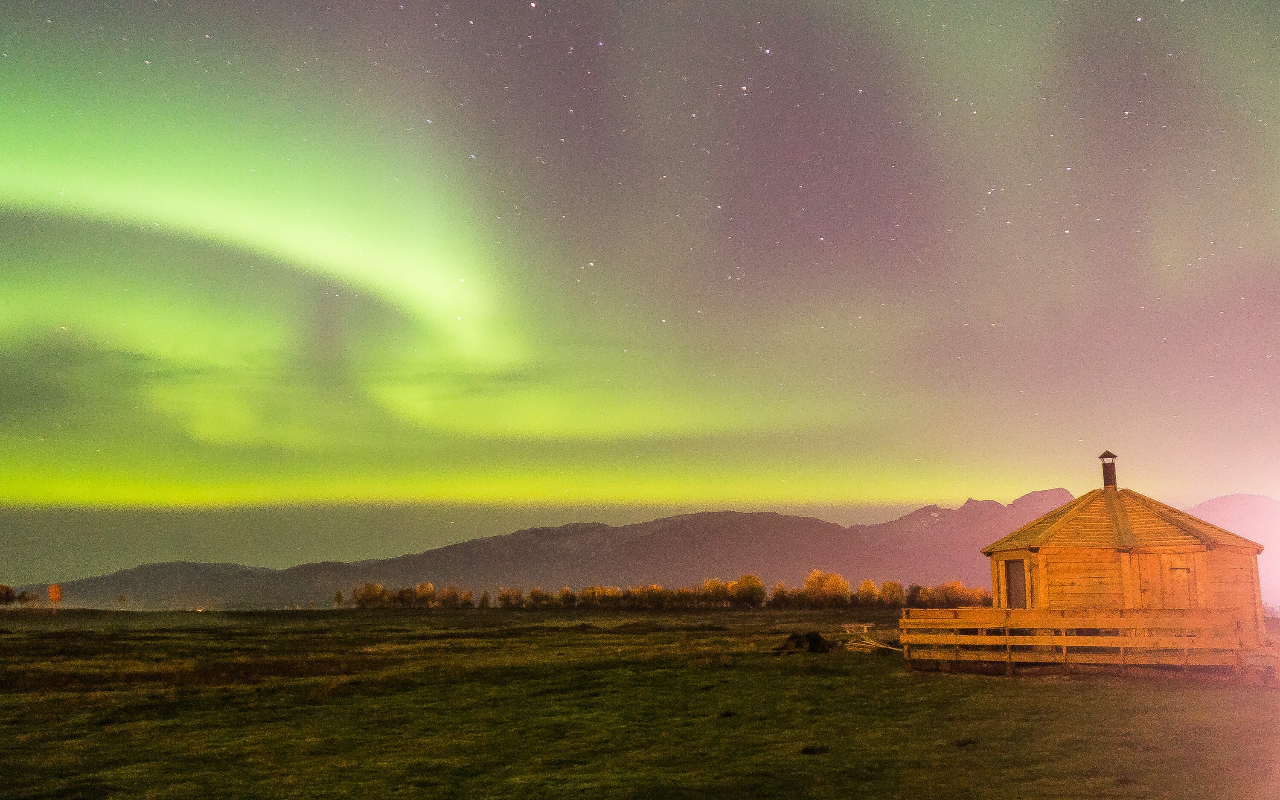 在遙遠的荒野景觀上，絢麗的北極光閃耀著，讓您沉浸在寧靜的北極氛圍中。