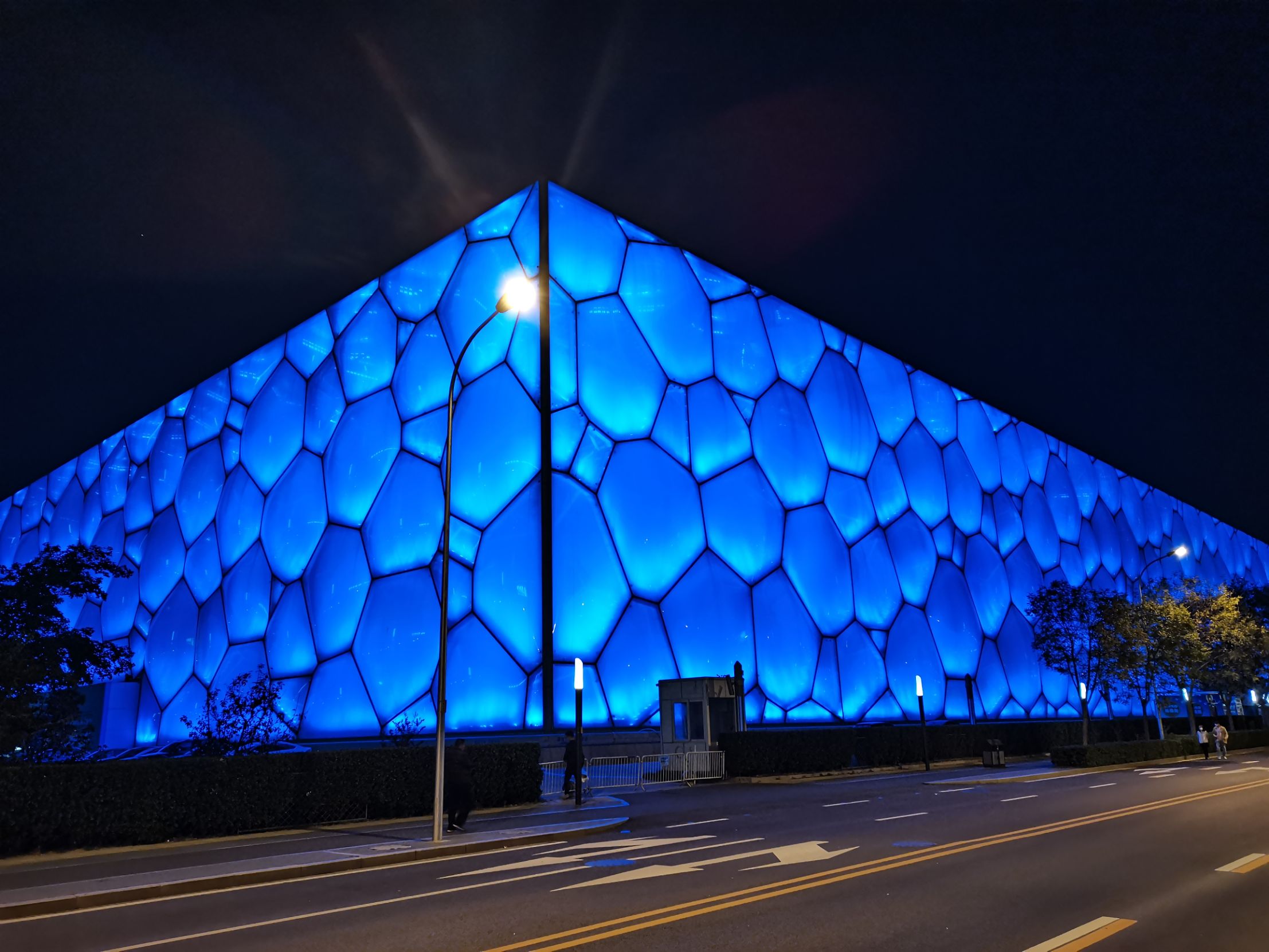 夜幕下，“鳥巢”在璀璨燈光的勾勒中，那獨特的編織狀外觀似繁星點綴的夢幻之巢，與周邊的燈火交相輝映，散發著現代建築的靈動與科技美感，宏偉而又迷人