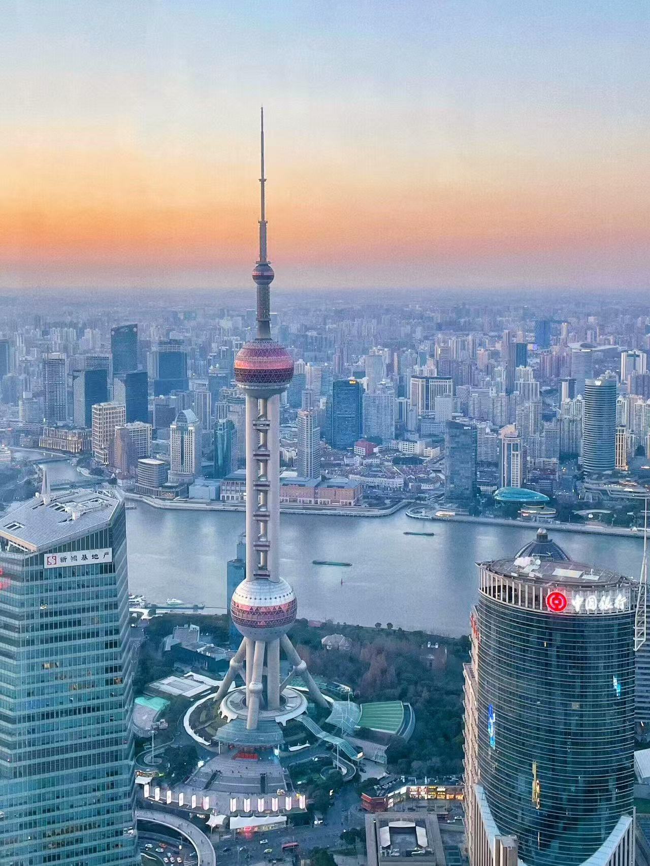 黃昏時分，東方明珠電視塔在暖調霞光中熠熠生輝，浦江兩岸高樓林立，江水蜿蜒流淌，錯落的城市建築鋪展成一幅絕美魔都天際線畫卷