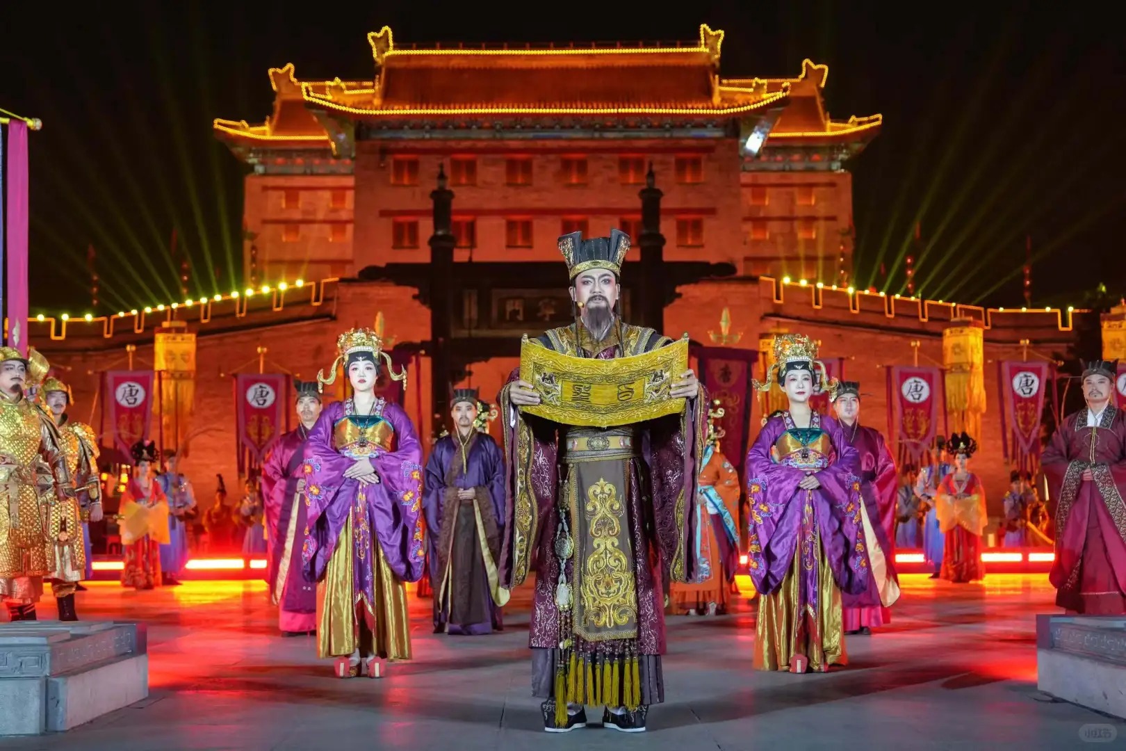 演員們身著精緻唐代服飾，中間演員手持金黃卷軸，頭戴冕冠，服飾華麗莊重