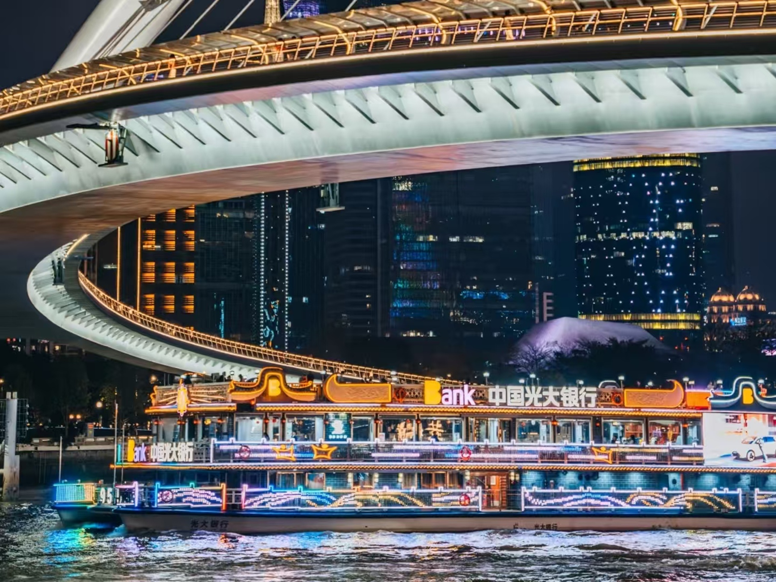 船身霓虹與 “Bank” 標識醒目,雙層甲板坐滿遊客,從海心橋下駛過,現代遊船與橋樑燈光構成動感夜景 船身霓虹與 “Bank” 標識醒目,雙層甲板坐滿遊客,從海心橋下駛過,現代遊船與橋樑燈光構成動感夜景