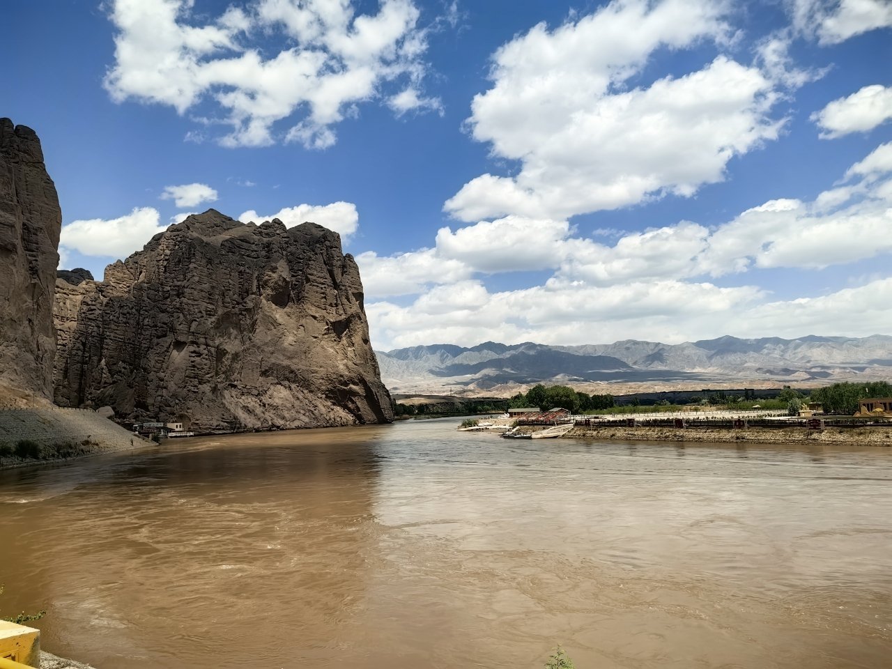 這是黃河石林景區。渾濁的棕黃色河水奔湧而過,水面寬闊,泛起層層漣漪,彰顯黃河水系的磅礴氣勢。左側鐵鏽色的巖壁陡然矗立,表面溝壑縱橫,紋理粗獷,似被歲月與流水共同雕琢。遠處山巒連綿起伏,與藍天白雲相接,構成開闊的天際線。河、石、山、天四者交融,既顯大自然的鬼斧神工,又透出原始野性的美感,令人心生敬畏。 這是黃河石林景區。渾濁的棕黃色河水奔湧而過,水面寬闊,泛起層層漣漪,彰顯黃河水系的磅礴氣勢。左側鐵鏽色的巖壁陡然矗立,表面溝壑縱橫,紋理粗獷,似被歲月與流水共同雕琢。遠處山巒連綿起伏,與藍天白雲相接,構成開闊的天際線。河、石、山、天四者交融,既顯大自然的鬼斧神工,又透出原始野性的美感,令人心生敬畏。