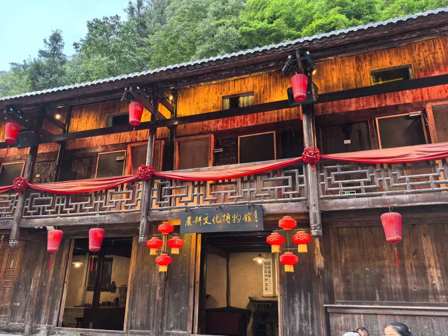 木質的 “農耕文化博物館” 在暖光中顯得格外親切，紅燈籠與紅綢帶交織出濃郁的民俗氣息。雕花的木欄與古樸的窗欞訴說著過往的農耕故事