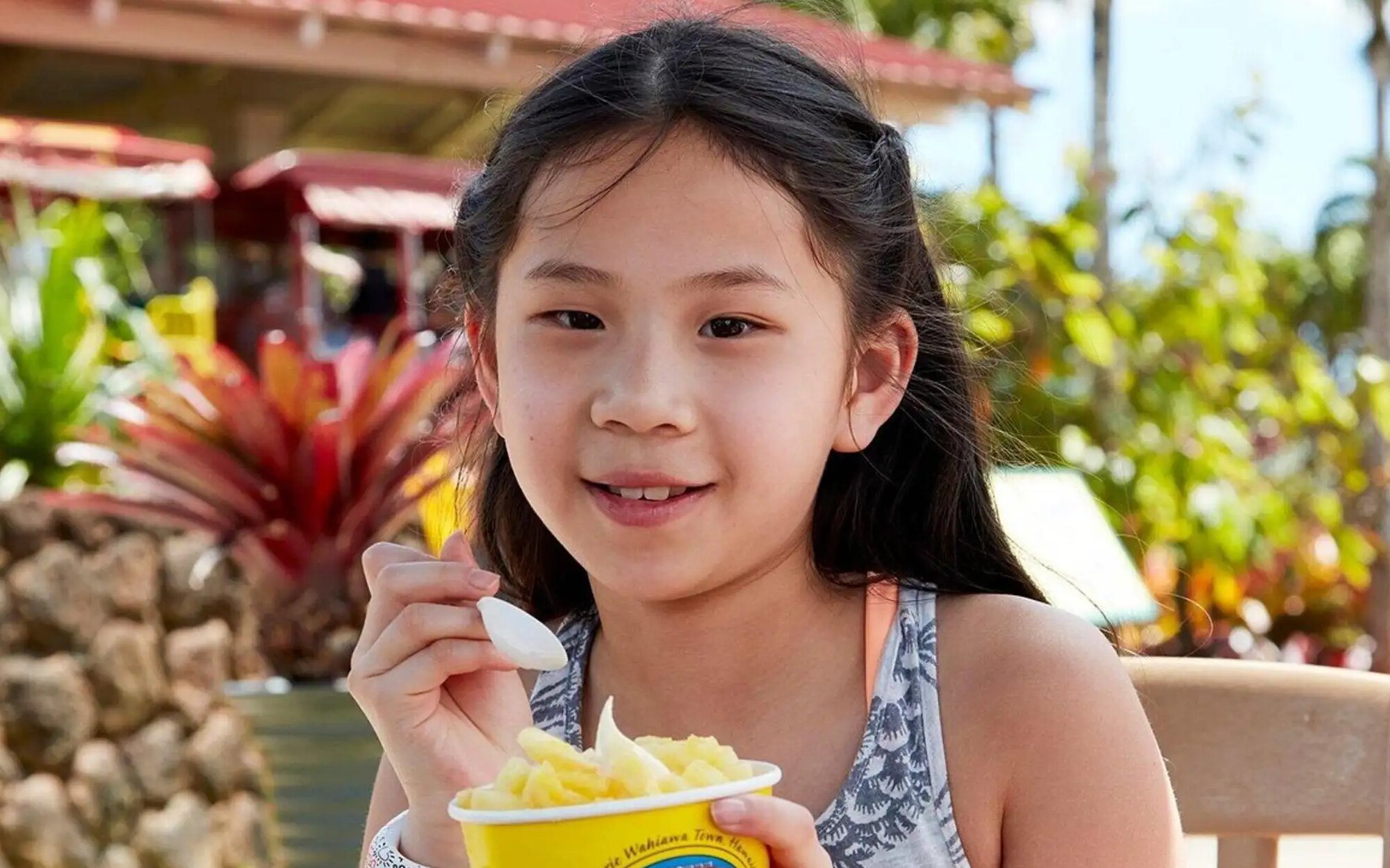 年輕遊客在歐胡島都樂鳳梨園的戶外花園中，手持鳳梨甜點入座