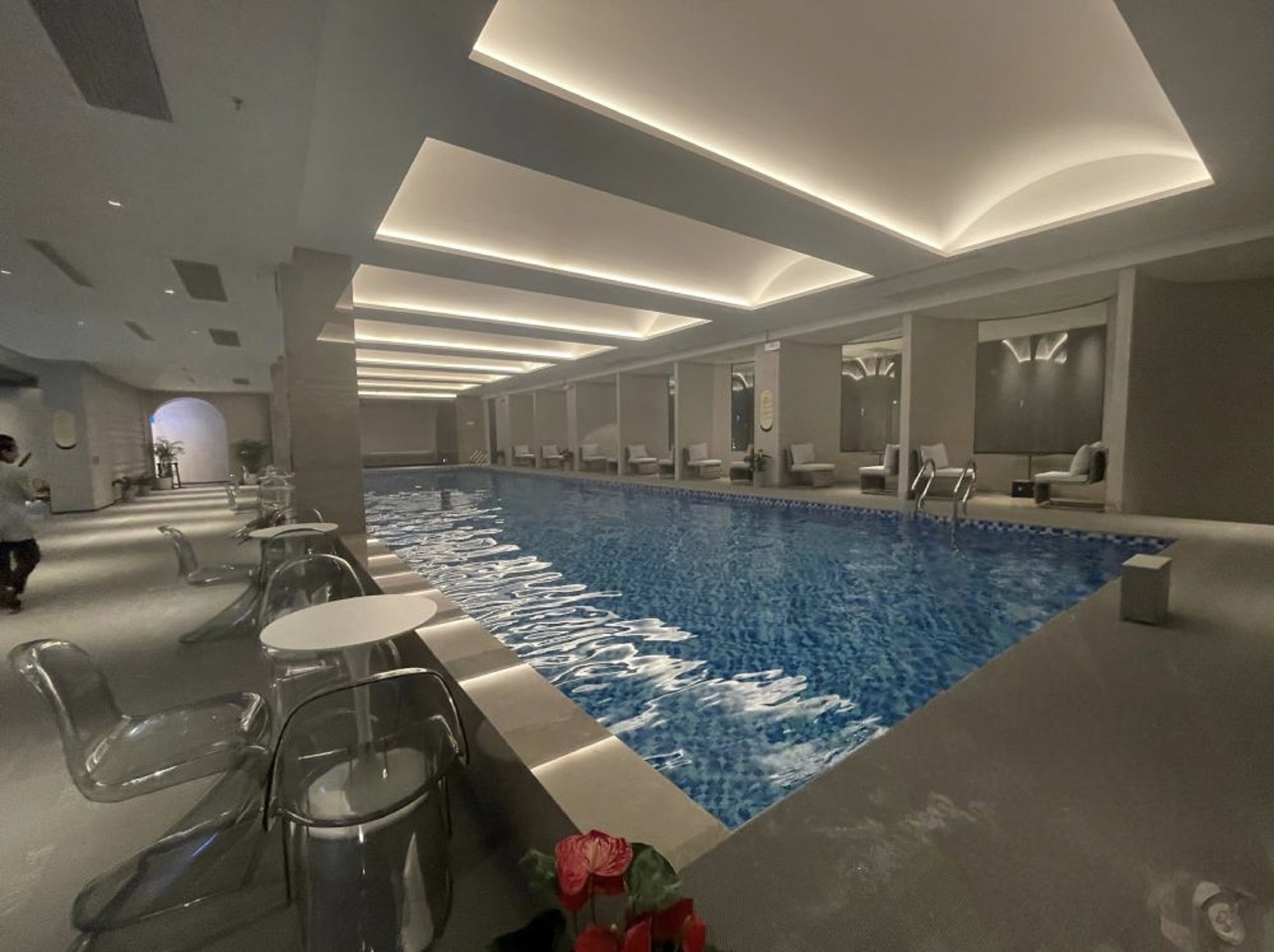 池邊一側擺放著透明桌椅,桌上有紅色花卉裝飾 池邊一側擺放著透明桌椅,桌上有紅色花卉裝飾