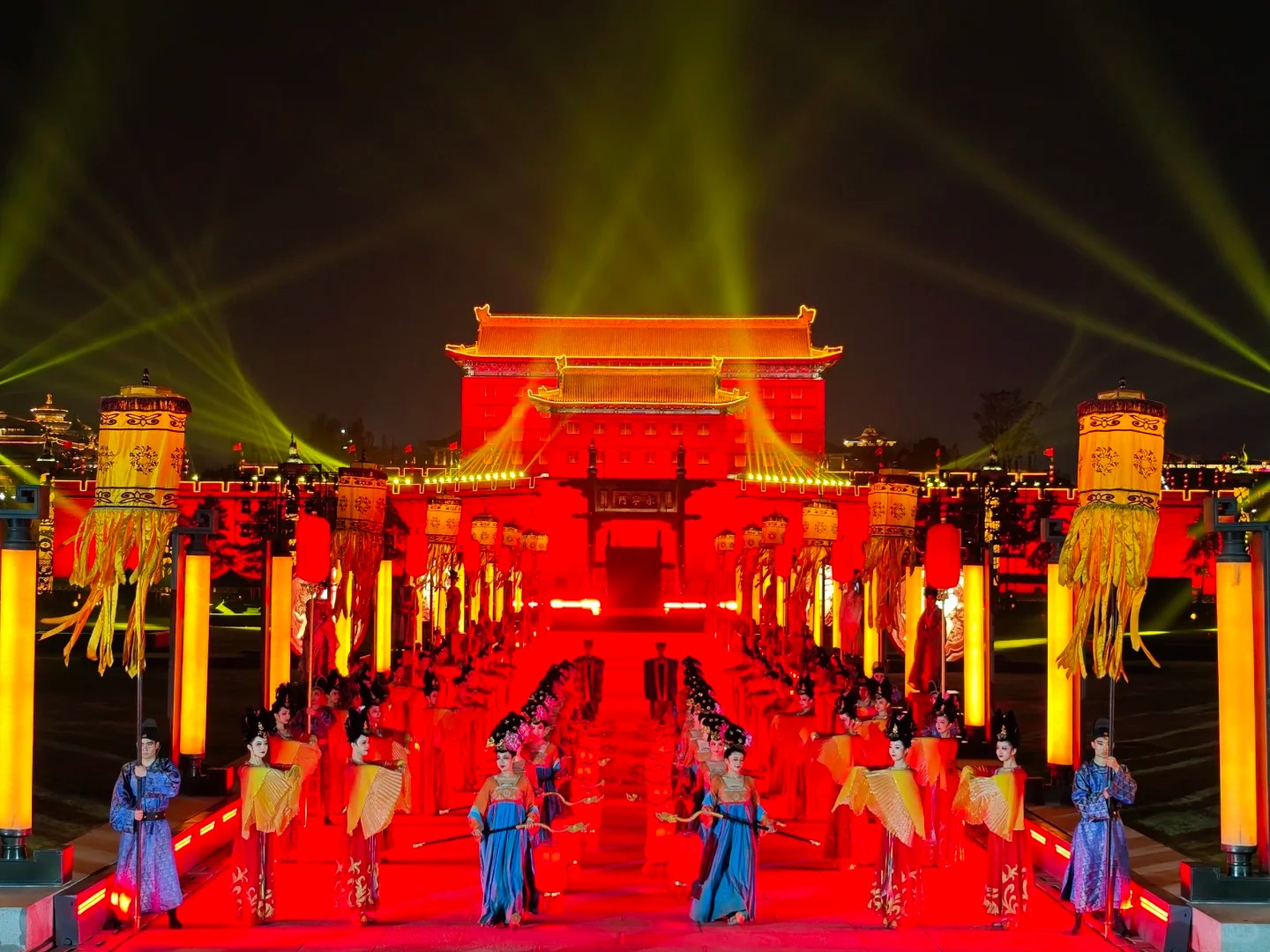 眾多身著唐代服飾的演員整齊排列兩側，場面宏大。古城牆在紅色燈光的映照下氣勢磅礴