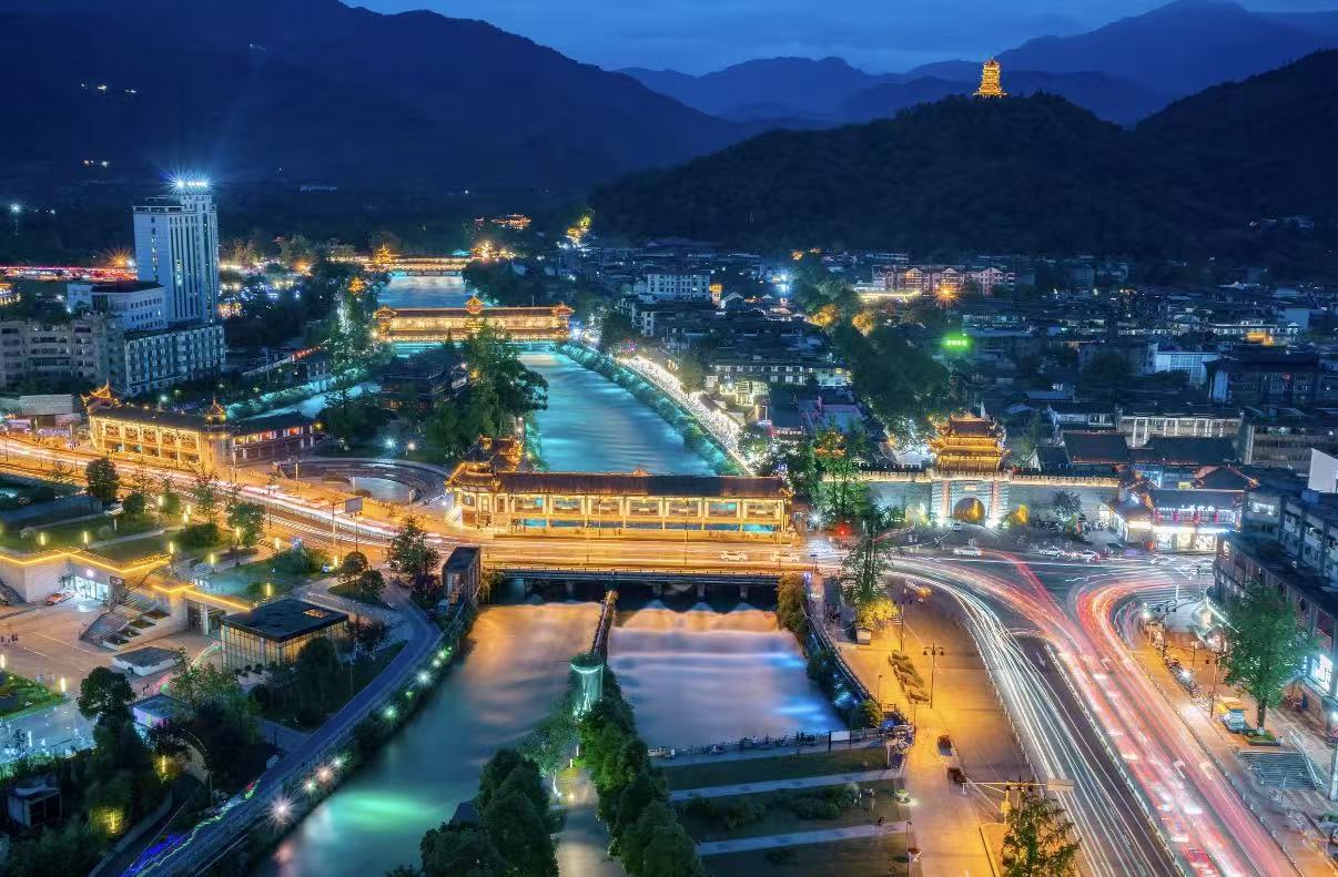 都江堰市區夜景俯瞰,河流穿城而過,廊橋燈火如鏈,車流光軌交織,遠山含黛,古塔隱於夜色,展現出古城夜生活的鮮活與雅緻 都江堰市區夜景俯瞰,河流穿城而過,廊橋燈火如鏈,車流光軌交織,遠山含黛,古塔隱於夜色,展現出古城夜生活的鮮活與雅緻