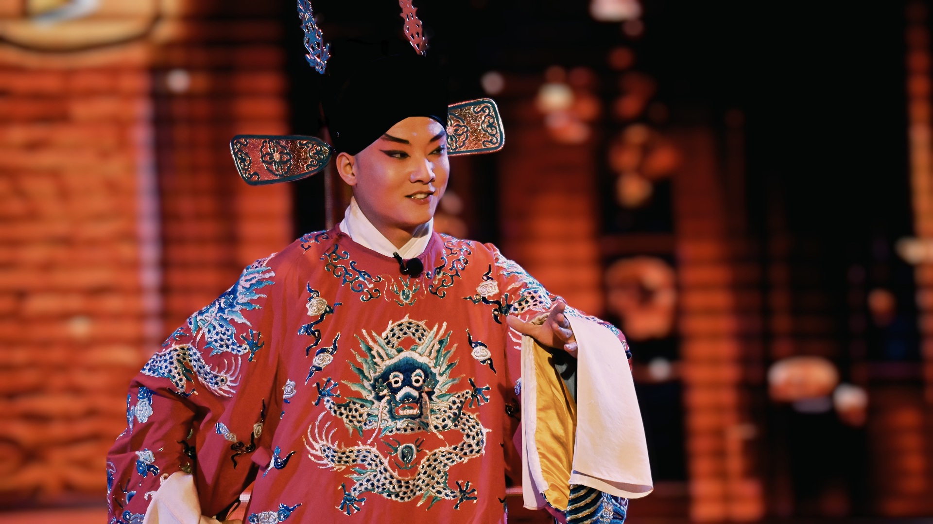 戲曲演員著紅袍，衣飾繡祥龍，戴烏紗帽，身姿舒展，背景暖光襯出傳統表演的雅緻