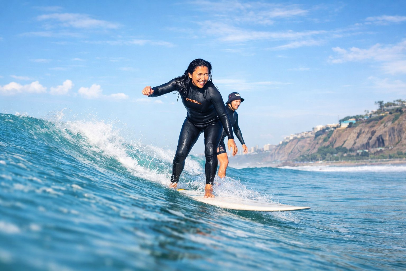 Confident surfer gliding across a turquoise wave at Playa Makaha with Miraflores coastline in the background.