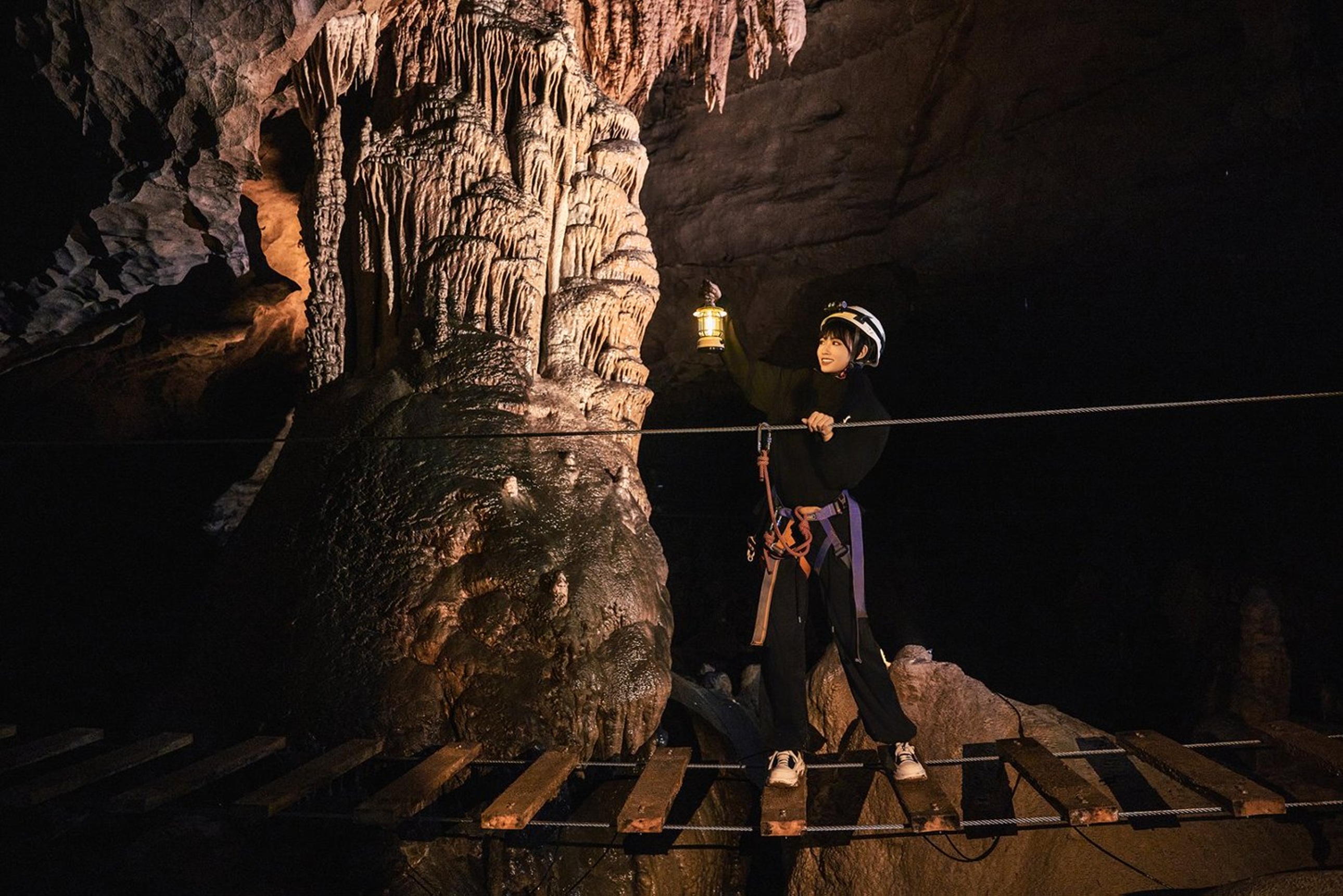 探險者持燈走在溶洞懸空木橋,身旁是億年形成的巨型鐘乳石,繩索與木板在光影裡晃動,每一步都充滿挑戰與驚喜 探險者持燈走在溶洞懸空木橋,身旁是億年形成的巨型鐘乳石,繩索與木板在光影裡晃動,每一步都充滿挑戰與驚喜