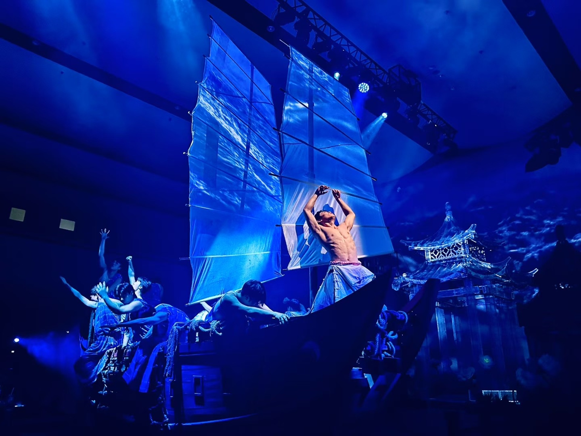 船型道具上，演員們配合展臂，藍帆與水紋光影交織，還原漁家勞作場景