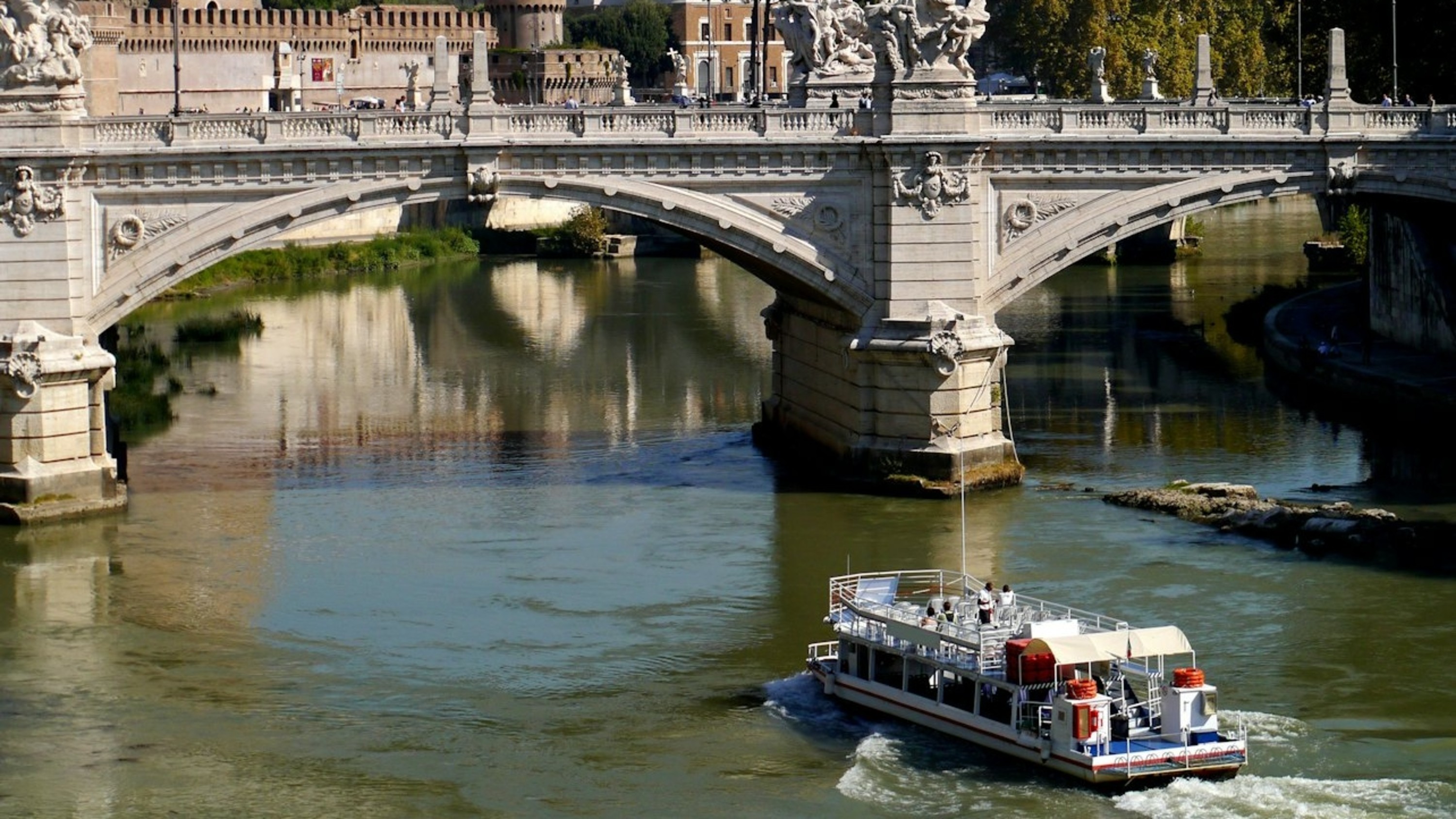 A close-up shot captures a boat smoothly cruising under an ancient stone bridge arch
