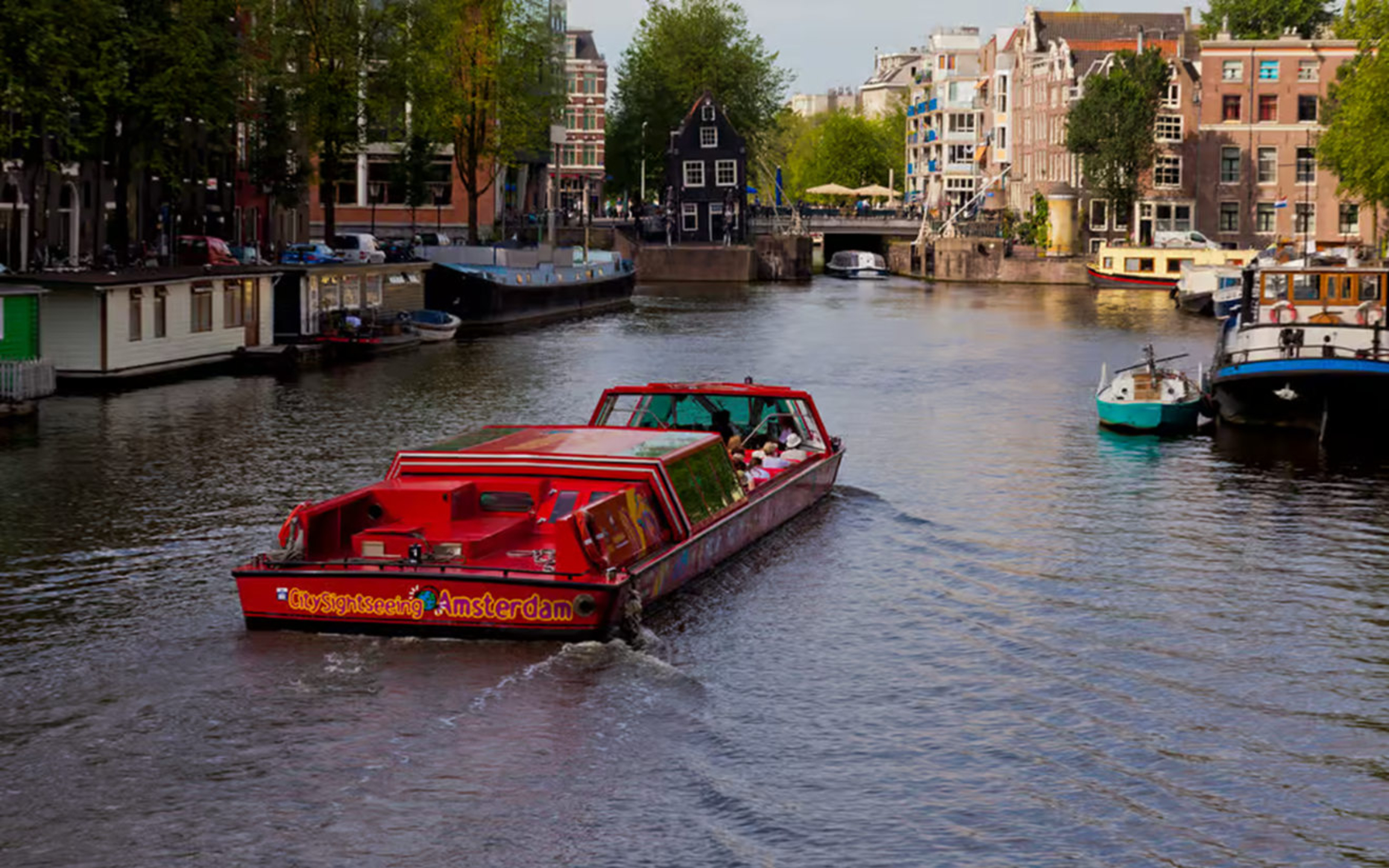 Hop-on hop-off sightseeing boat gliding through Amsterdam canals beneath charming historic canal houses
