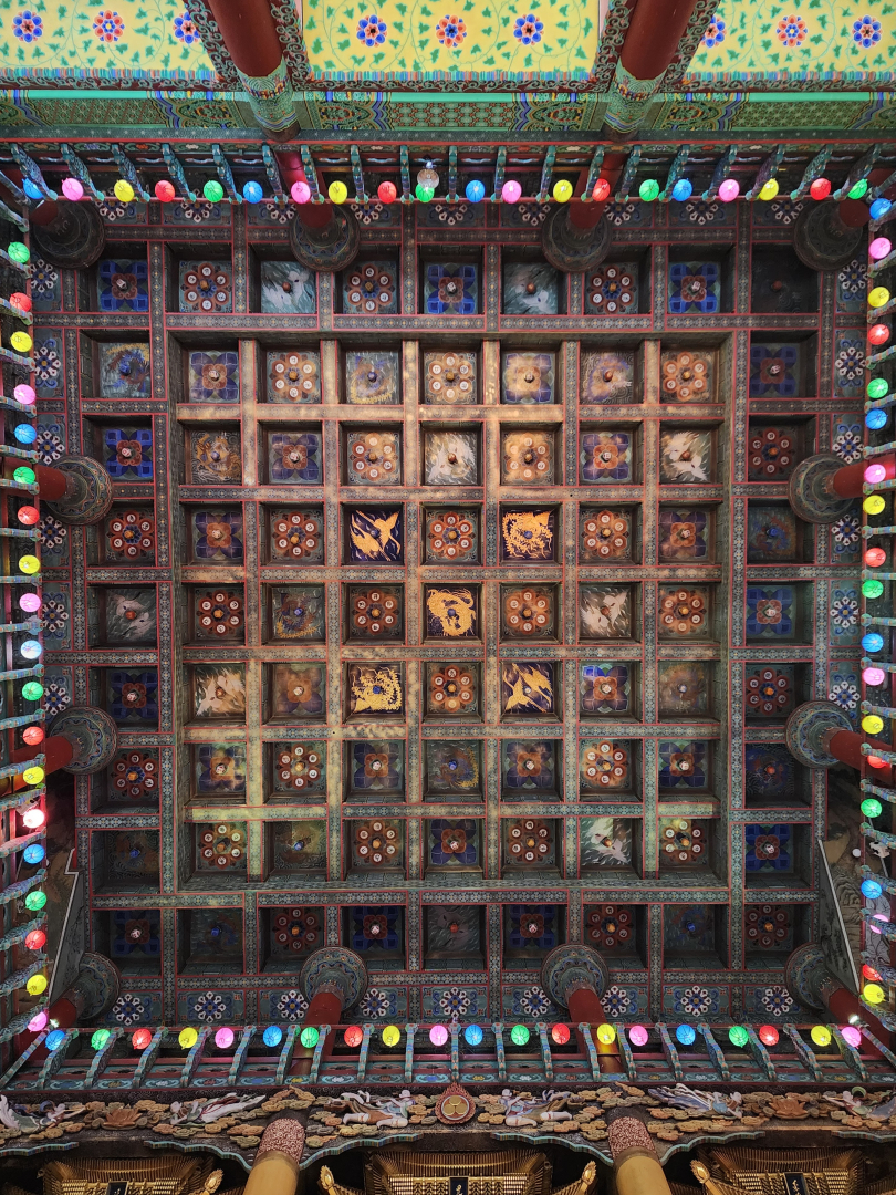 The ornate ceiling of Yakcheonsa Temple's main hall is a masterpiece of vibrant colors and symbolism, inviting you to look up and reflect in awe.