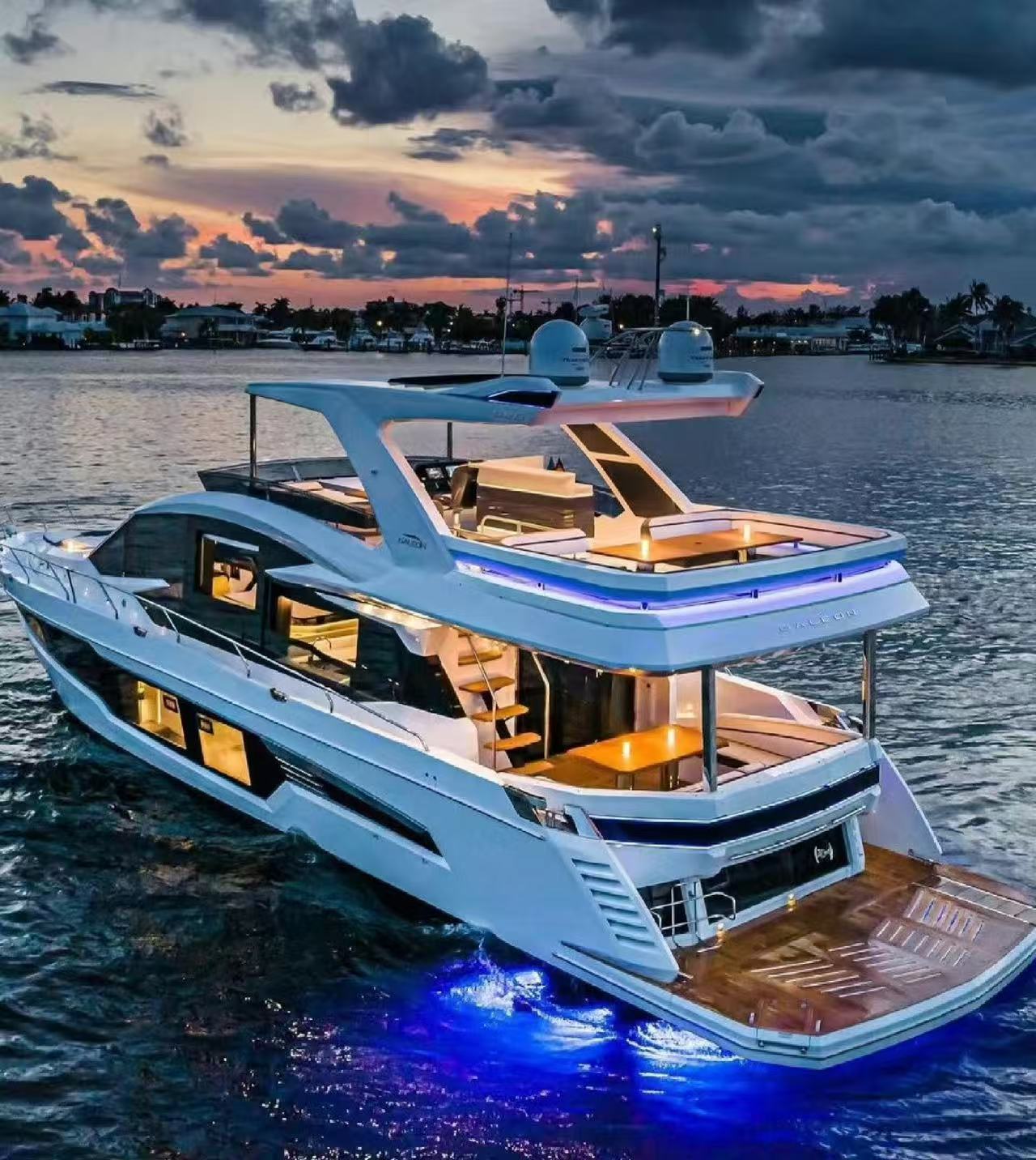 黃昏時分，一艘設計現代的白色豪華遊艇停泊在江面，船身線條流暢，三層甲板通透開闊。船底藍色燈光映亮江水，晚霞漫天的天空與遊艇暖黃內飾相映，盡顯奢華愜意的海上休閒氛圍