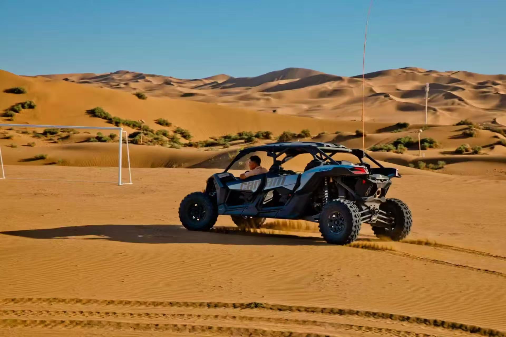 金色沙漠上，一輛 UTV 全地形車飛馳，揚起細沙，背景是連綿沙丘，場地還有沙漠球門，充滿狂野的沙漠玩樂氣息