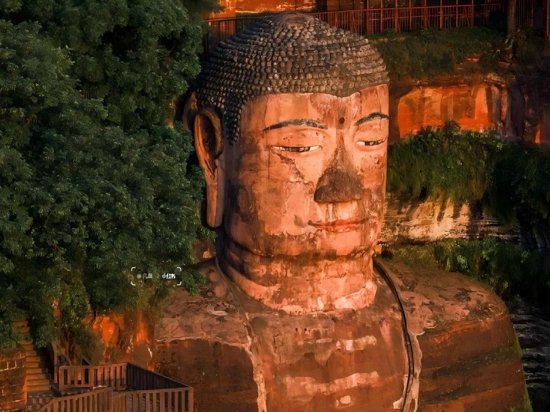 遠眺夕陽下的樂山大佛，佛像上鍍上柔光，古樸石身刻滿歲月痕跡，蔥蘢綠意環伺，盡顯千年沉靜莊嚴。