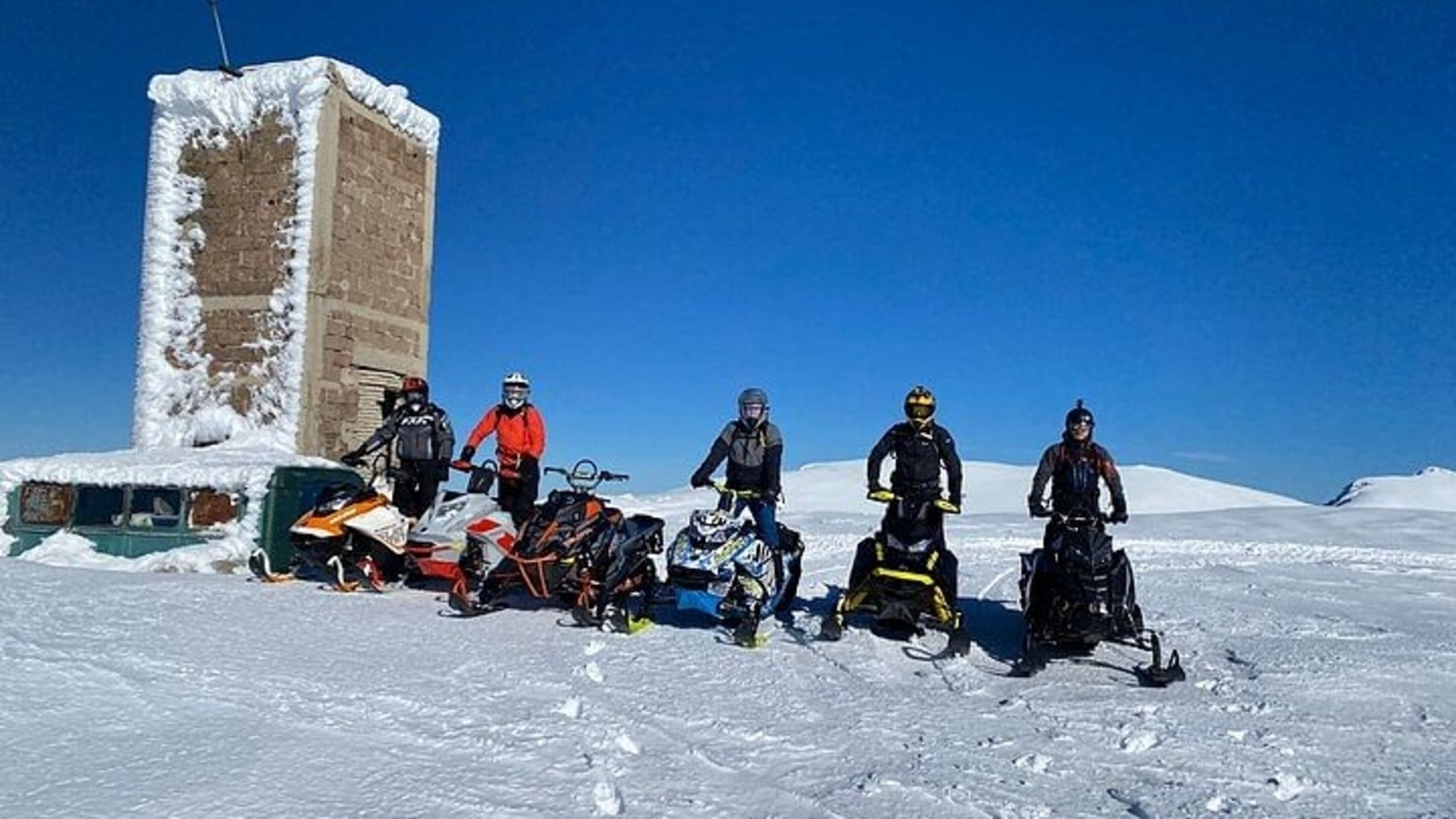 A cheerful group poses with snowmobiles, surrounded by fresh, untouched snow everywhere