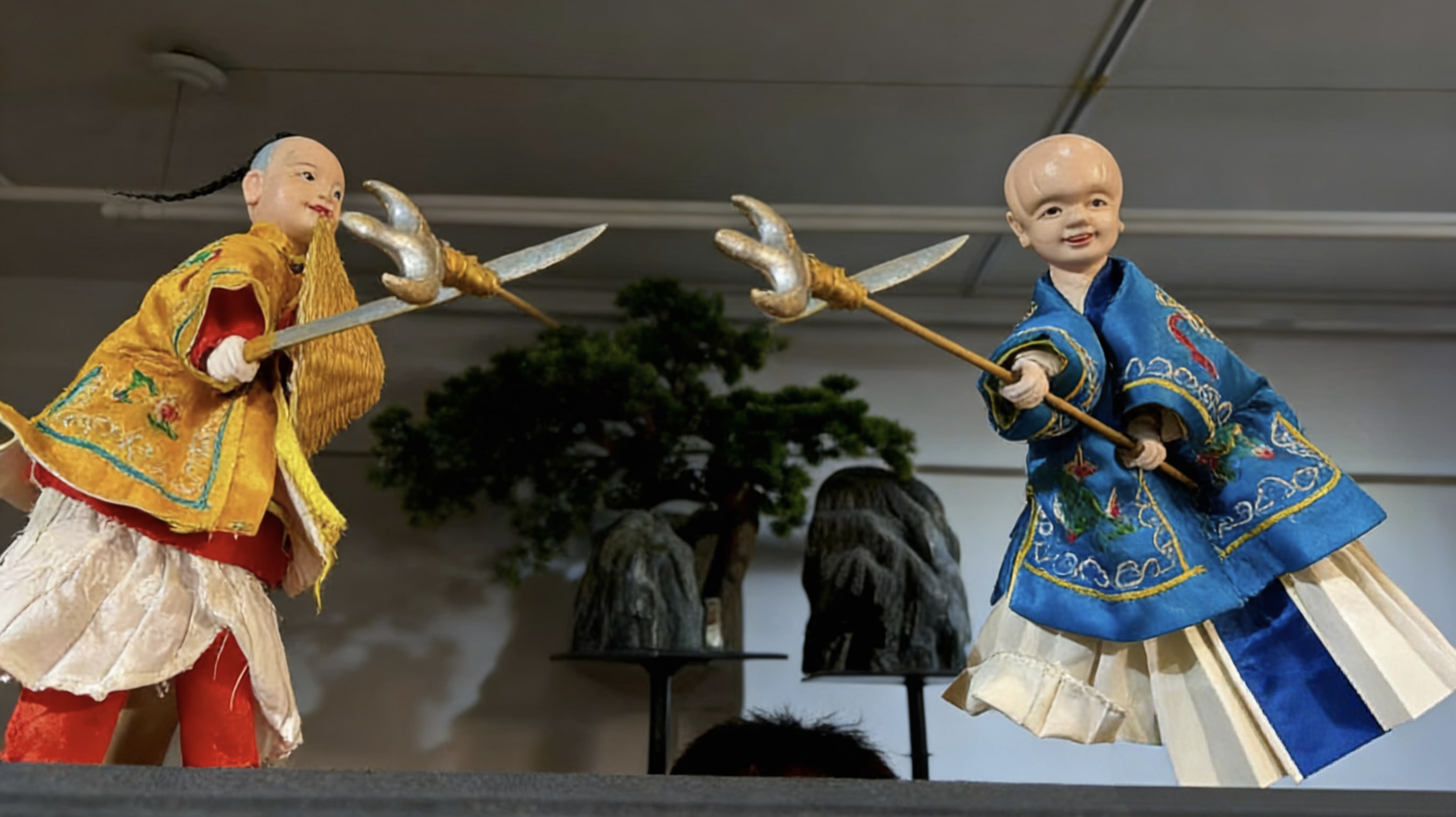 袖角的彩繡跟著抖出細碎的光。它們圓臉上的笑意憨態可掬，卻在藝人的指尖裡，演活了江湖快意