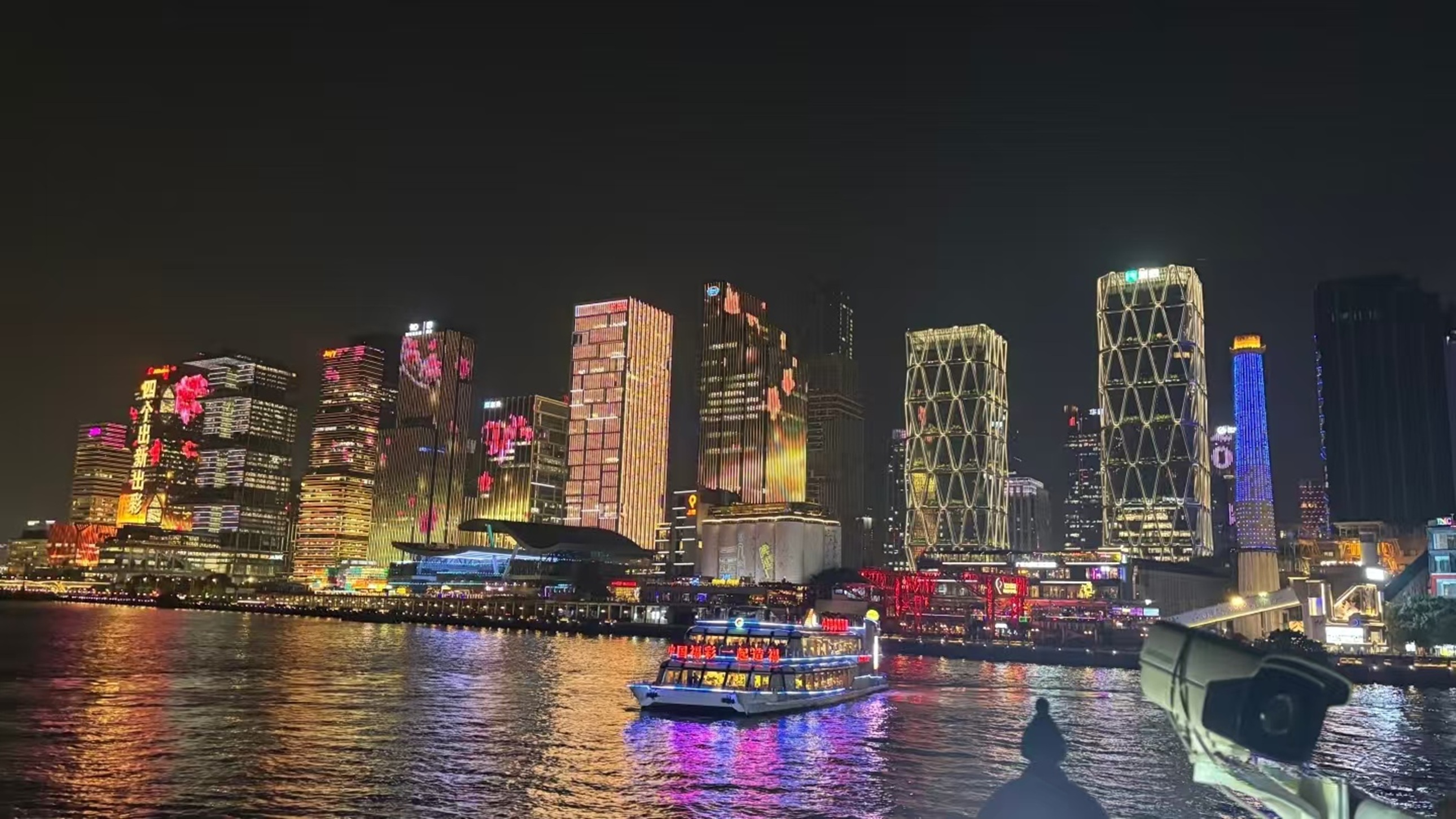 遊船穿梭江面,兩岸高樓幕牆亮起燈光秀,“四個出新出彩” 標語與絢爛光影交織,城市繁華與江景倒影相映成趣 遊船穿梭江面,兩岸高樓幕牆亮起燈光秀,“四個出新出彩” 標語與絢爛光影交織,城市繁華與江景倒影相映成趣