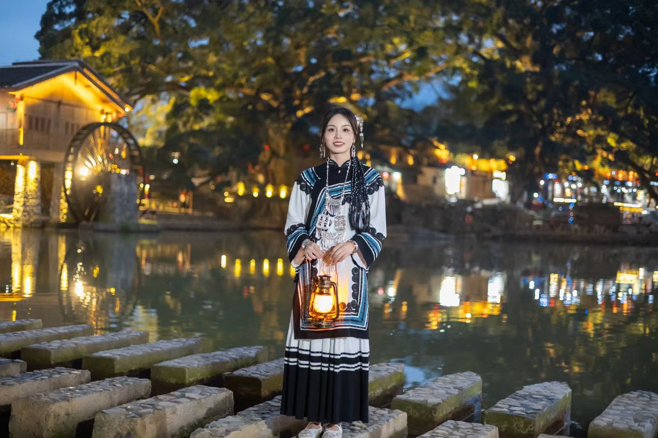 夜色中的石跳橋上,身著黎風服飾的姑娘手持燈籠靜立 夜色中的石跳橋上,身著黎風服飾的姑娘手持燈籠靜立