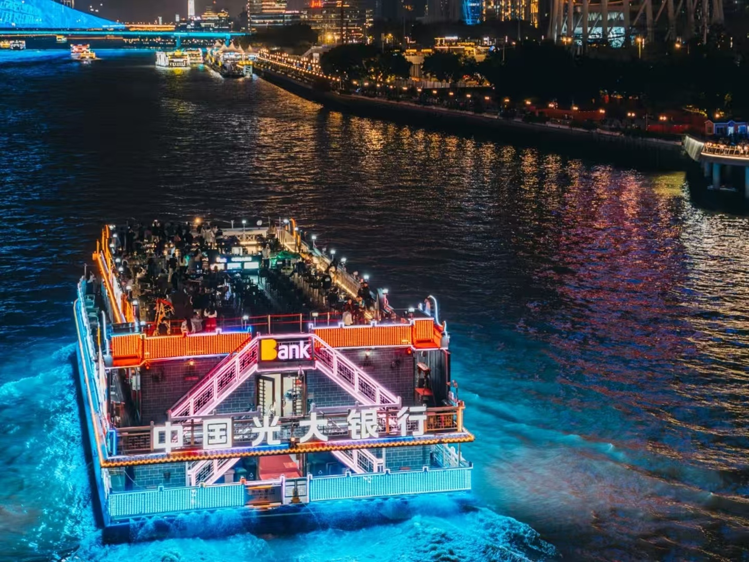 小型遊船泛著藍黃燈光掠過橋底,橋上行人駐足觀景,背景建築大屏與橋身燈光呼應,夜遊互動感拉滿 小型遊船泛著藍黃燈光掠過橋底,橋上行人駐足觀景,背景建築大屏與橋身燈光呼應,夜遊互動感拉滿
