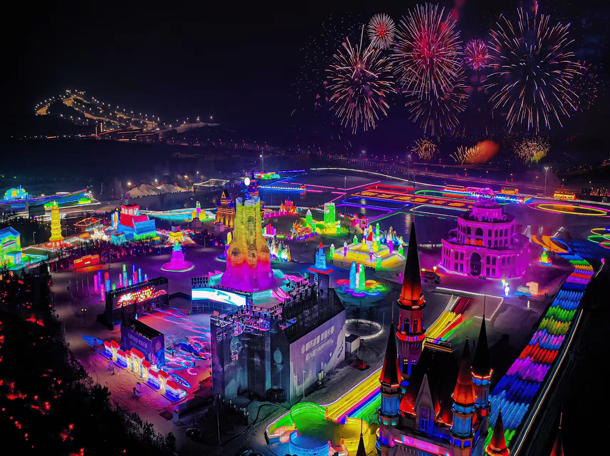 長春冰雪新天地夜景航拍,冰雕建築群被七彩燈光裹滿,煙火在夜空綻放,遊人穿梭其間,整個場地如夢幻的冰雪狂歡場 長春冰雪新天地夜景航拍,冰雕建築群被七彩燈光裹滿,煙火在夜空綻放,遊人穿梭其間,整個場地如夢幻的冰雪狂歡場
