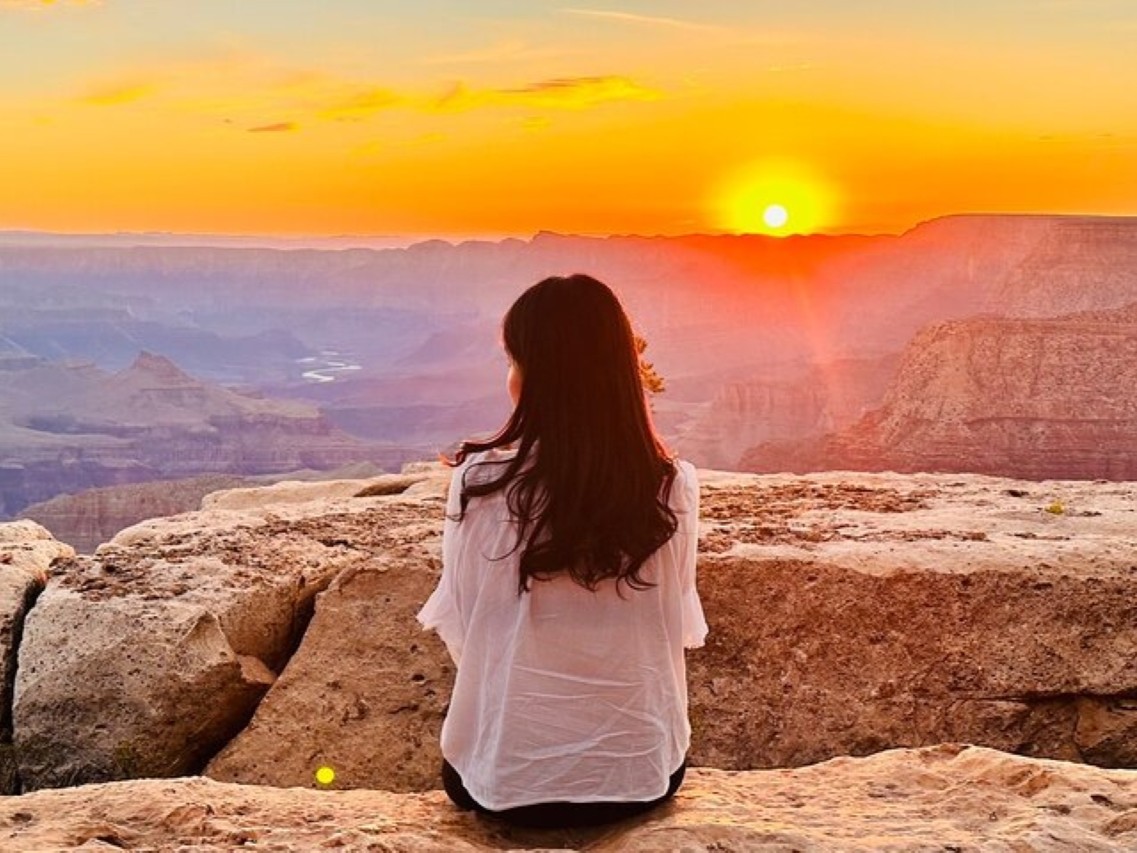 A woman feels the thrill sitting on the canyon rim during a breathtaking Grand Canyon sunrise