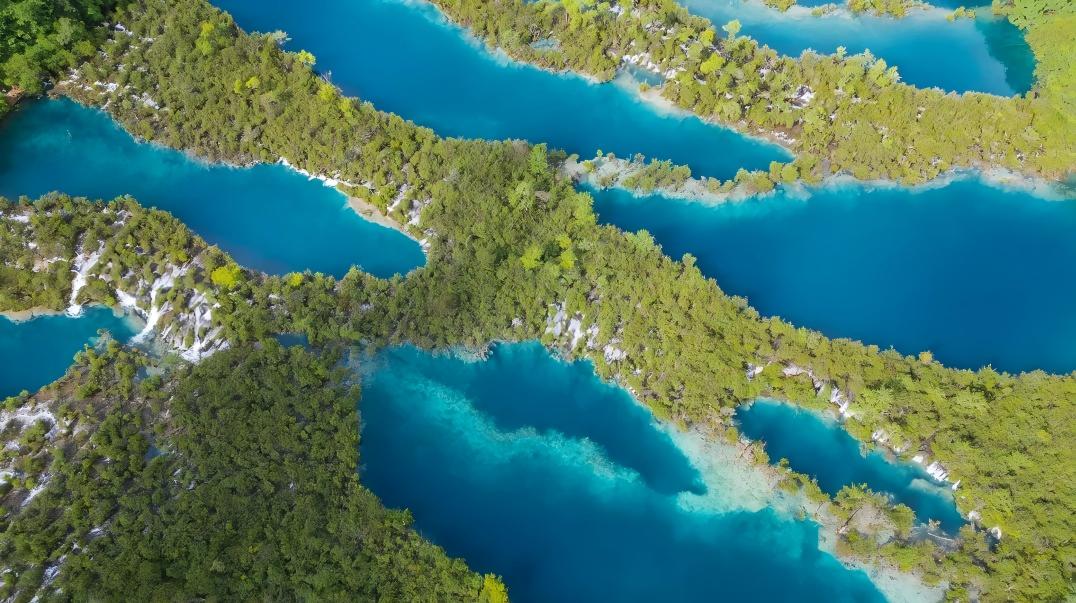 樹正群海：九寨門戶的梯田式海子群，19 個碧藍海子層層疊疊，上下高差近百米。湖水翻堤穿林，疊瀑銀浪飛濺，棧橋橫跨淺灘，藏式磨坊與轉經房點綴其間，樹在水中生、水在林間流，是九寨山水與人文的縮影。