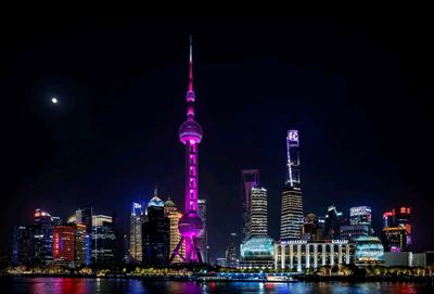 上海外灘的夜景，東方明珠塔被粉色燈光點亮，在黑夜中格外醒目，周圍的摩天大樓也燈光璀璨，黃浦江水面倒映著兩岸的光影