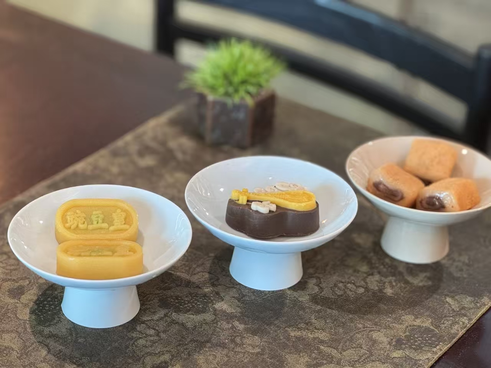 三款精緻茶點，造型小巧，擺於白碟，與綠植相襯，盡顯雅緻