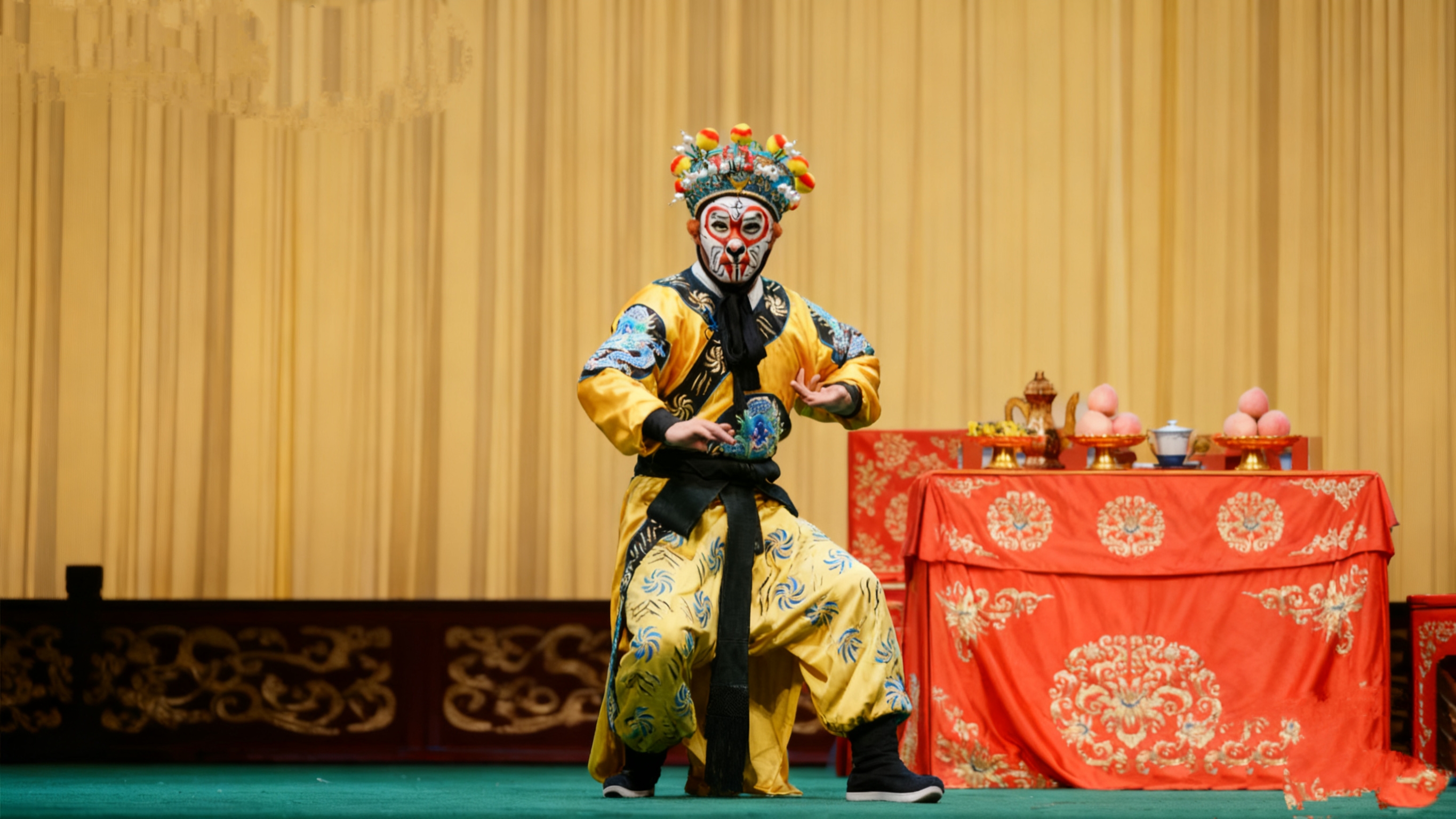 京劇演員飾演的美猴王在舞臺上表演,背景的黃色幕布與紅色的桌布形成鮮明對比,桌上的茶具與壽桃道具增添了場景的真實感,將觀眾帶入了孫悟空大鬧天宮的經典情節中 京劇演員飾演的美猴王在舞臺上表演,背景的黃色幕布與紅色的桌布形成鮮明對比,桌上的茶具與壽桃道具增添了場景的真實感,將觀眾帶入了孫悟空大鬧天宮的經典情節中