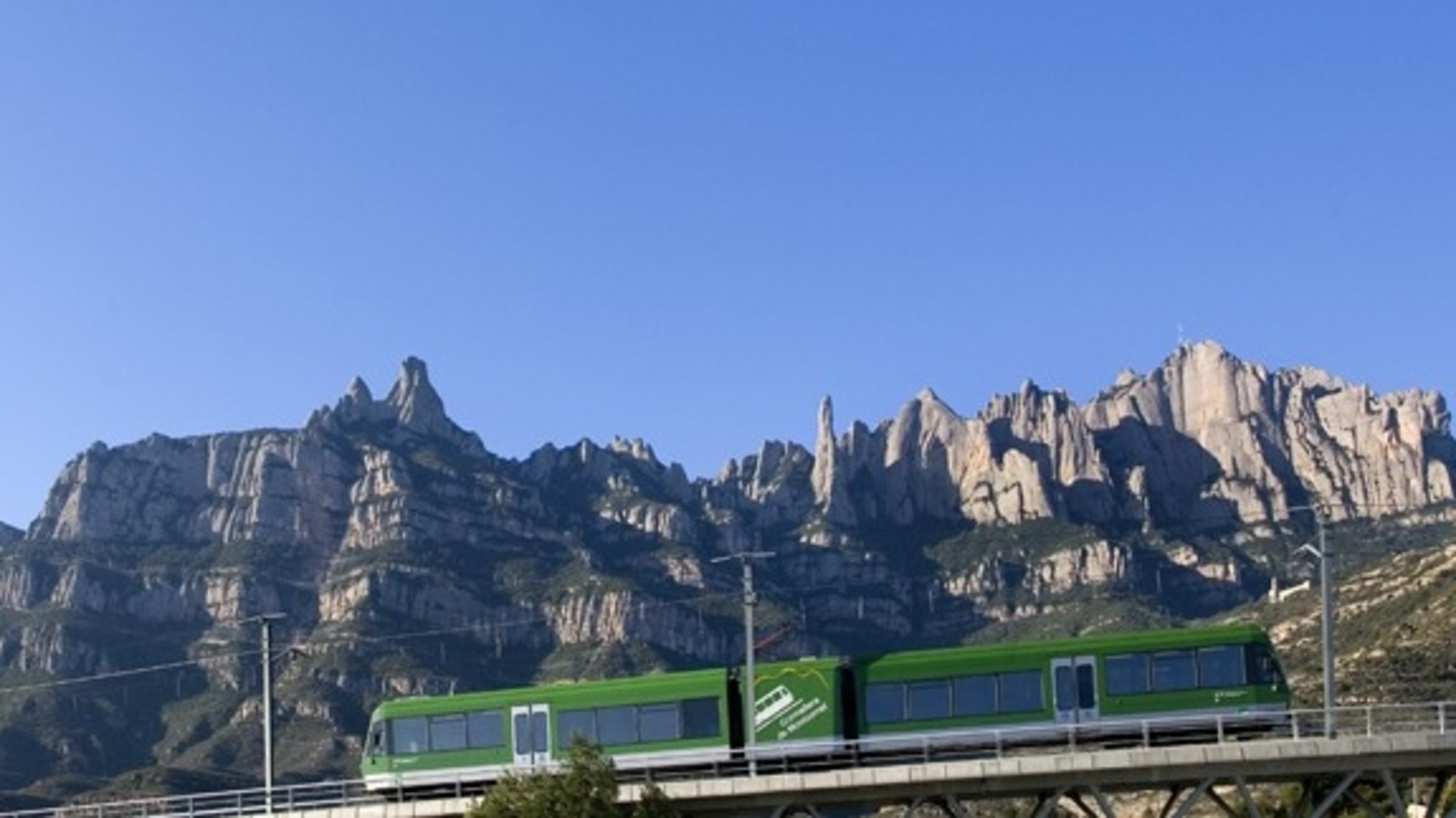 A scenic train approaches Montserrat with dramatic mountain peaks rising in the distance