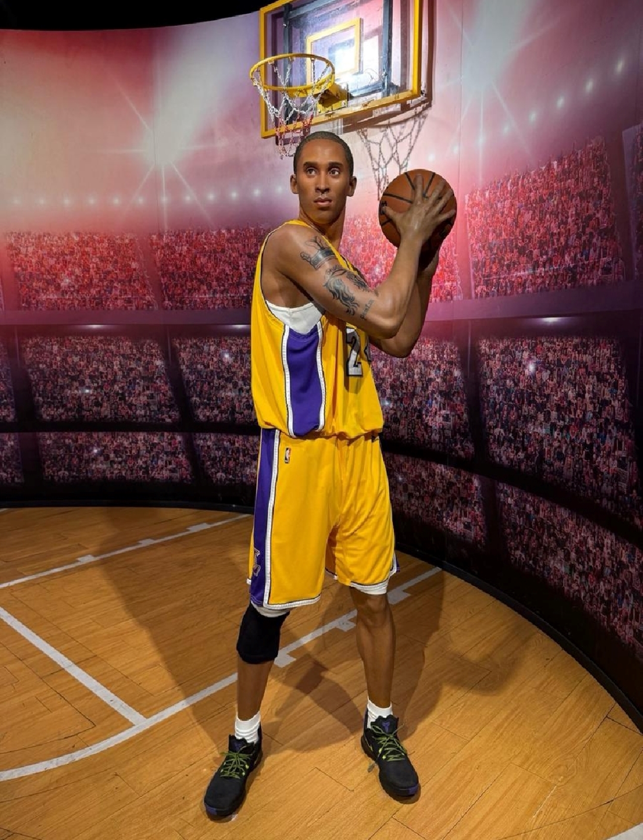 Kobe Bryant's wax figure recreates the moment when he holds the ball and prepares to shoot on the basketball court. The classic Lakers jersey is matched with the stadium background to commemorate this basketball legend.