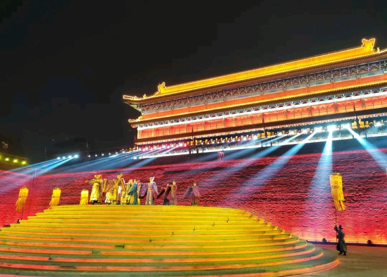 古城牆在燈光的照射下呈現出紅色與黃色的光影效果，幾束探照燈光劃破夜空，給畫面增添了層次感和神秘感