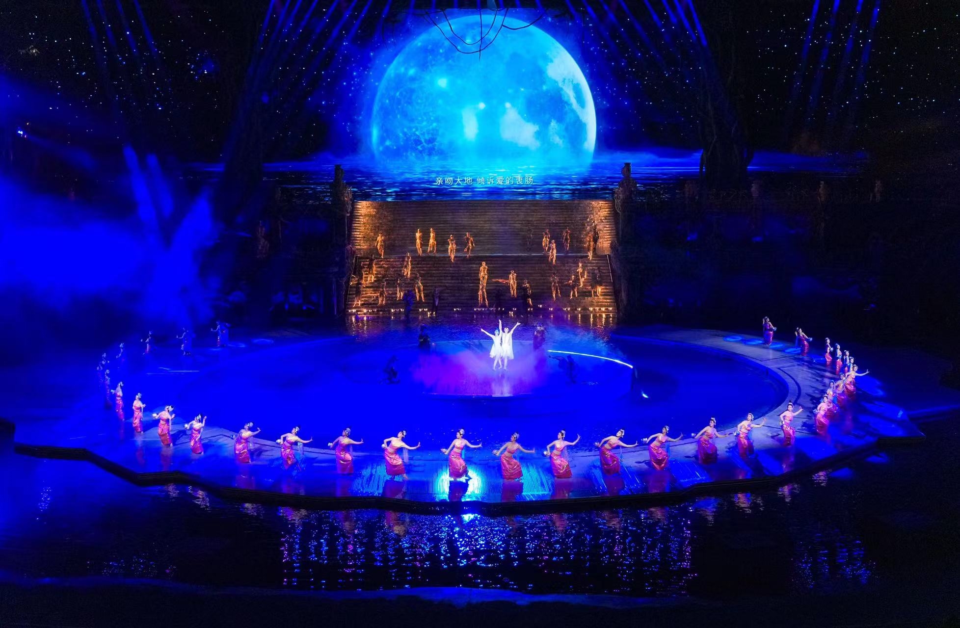 一輪巨大的藍色月亮為背景,演員圍成圈,中間有演員獨舞 一輪巨大的藍色月亮為背景,演員圍成圈,中間有演員獨舞