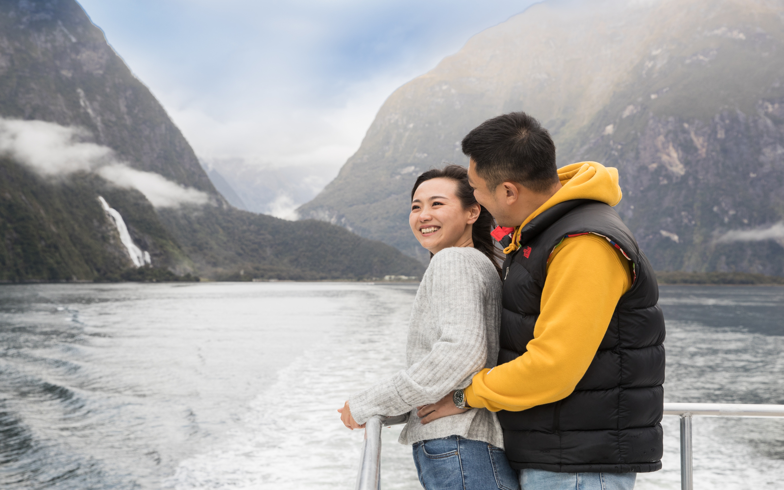 幸福的一家人在甲板上擺姿勢，他們的郵輪在米爾福德峽灣平靜的水域中滑行