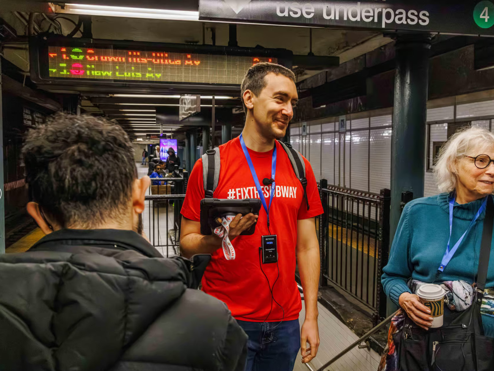 Tour group listens intently to subway history inside dimly lit vintage tiled station