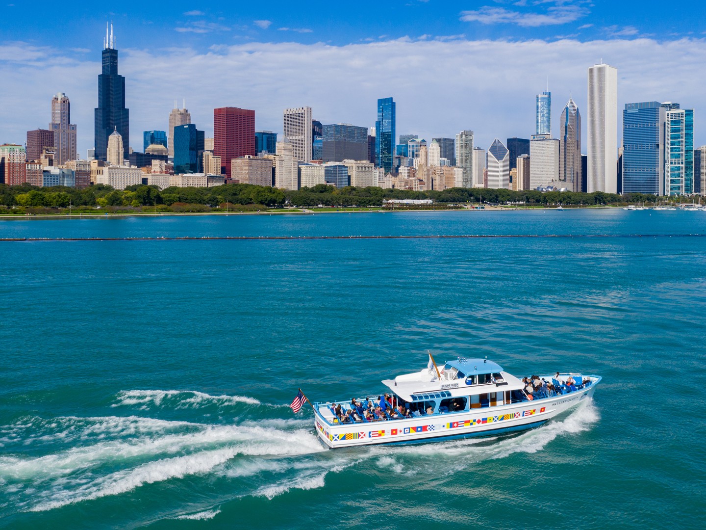 Tour boat cruising along Chicago River, surrounded by towering skyscrapers under clear blue skies