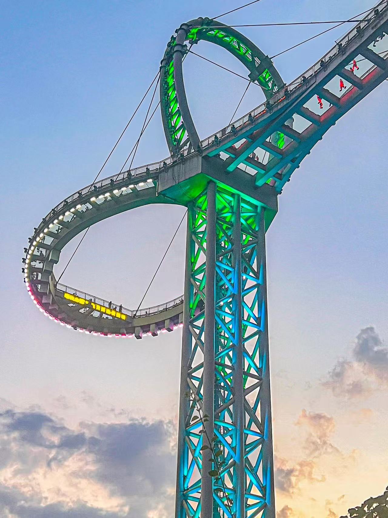 夜幕下的天門懸廊超震撼！巨型環形玻璃橋被藍綠霓虹點亮，鋼結構支架科技感拉滿，懸廊上人影綽綽，晚霞作伴，是黃騰峽絕美的高空夜景打卡點