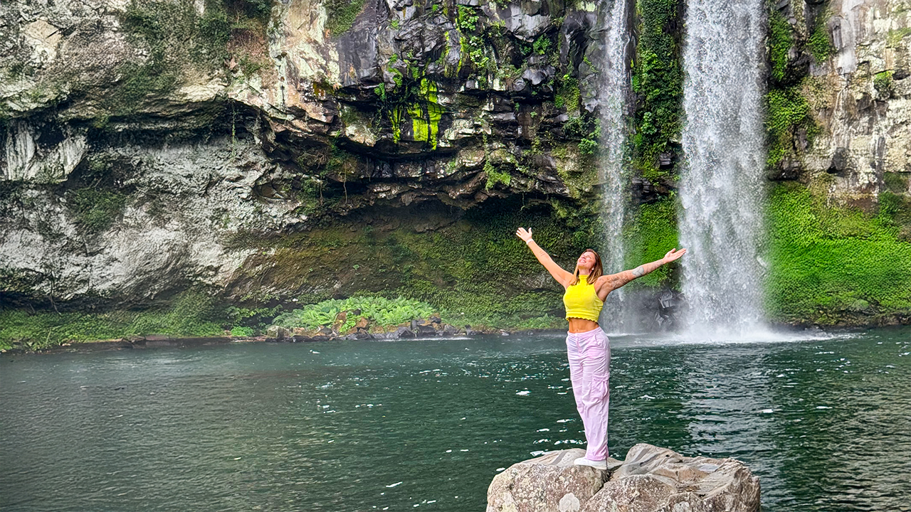 A serene waterfall hidden within lush forest, where clear water and volcanic rock create a calm and refreshing atmosphere.